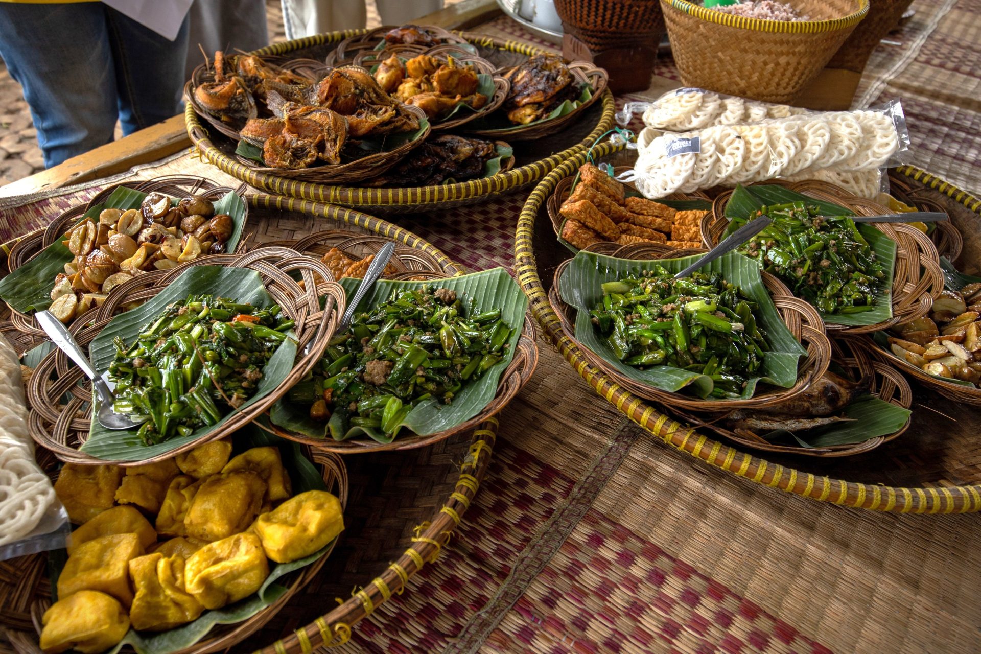 Woven baskets of cooked vegetables and sides laid out on a mat