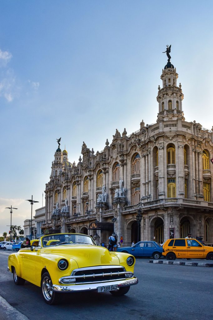Yellow vintage car parked in front of a grand Havana building