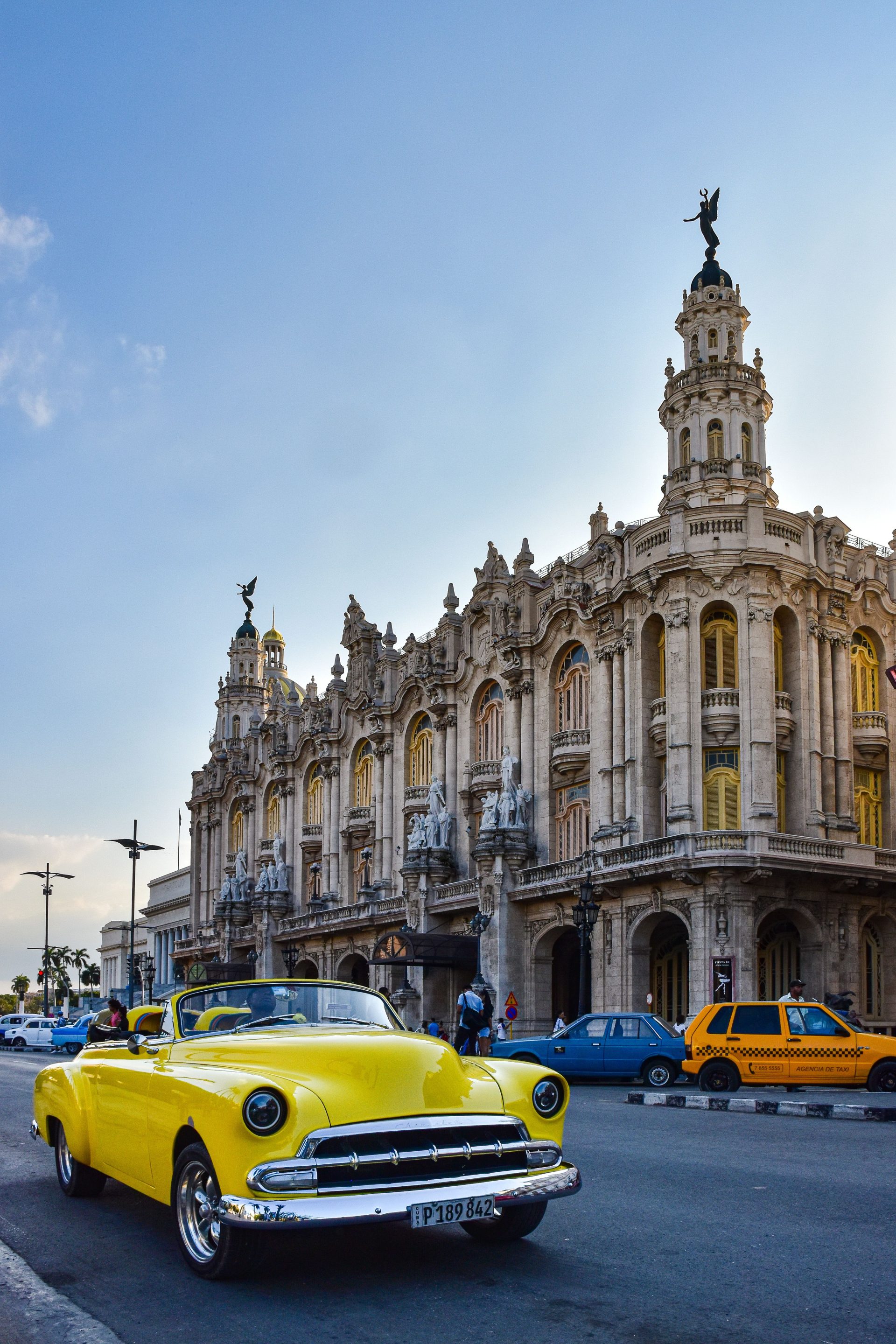 A yellow vintage car parked in front of a grand Havana building