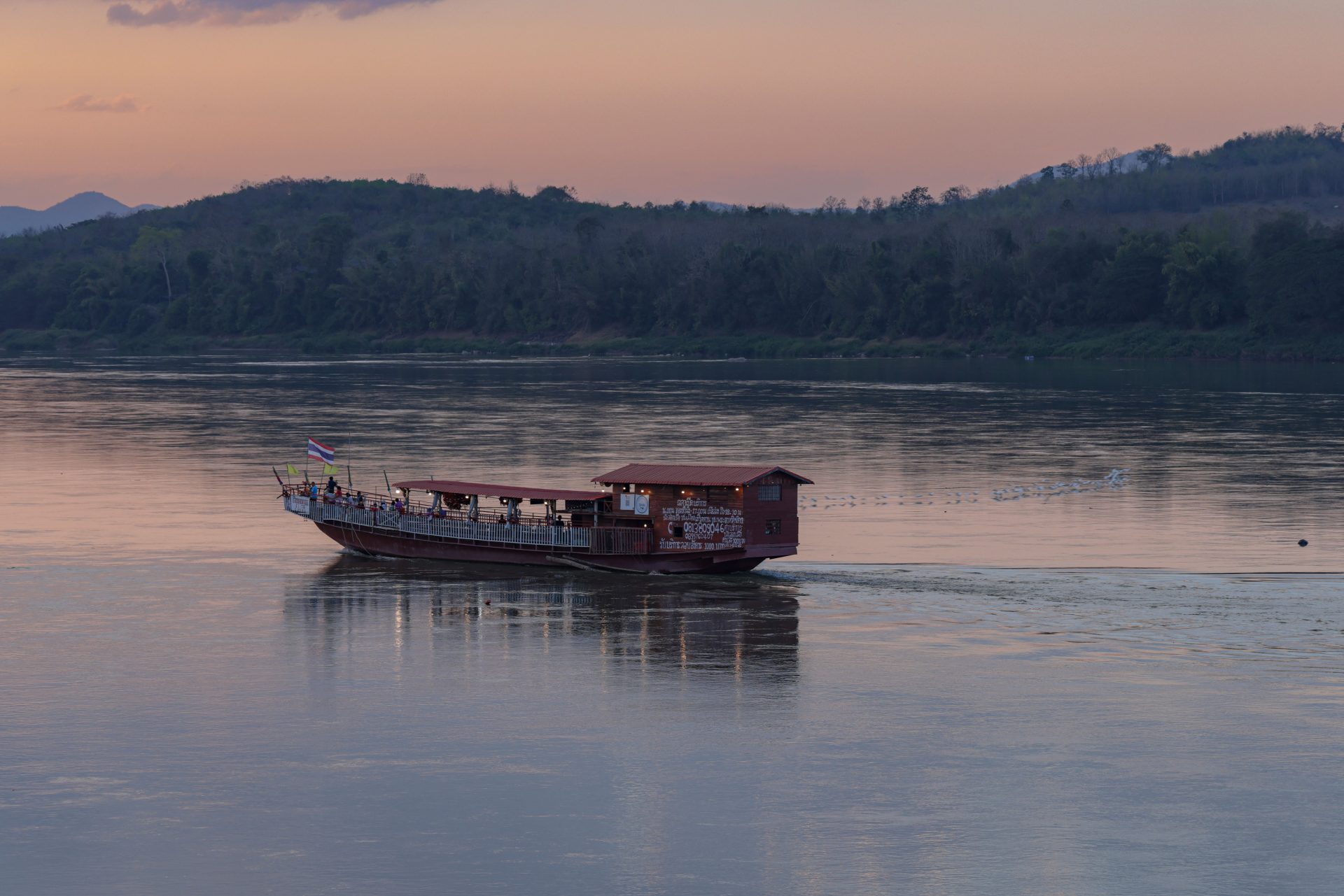 A boat on a wide river at dusk, hills fading behind it.