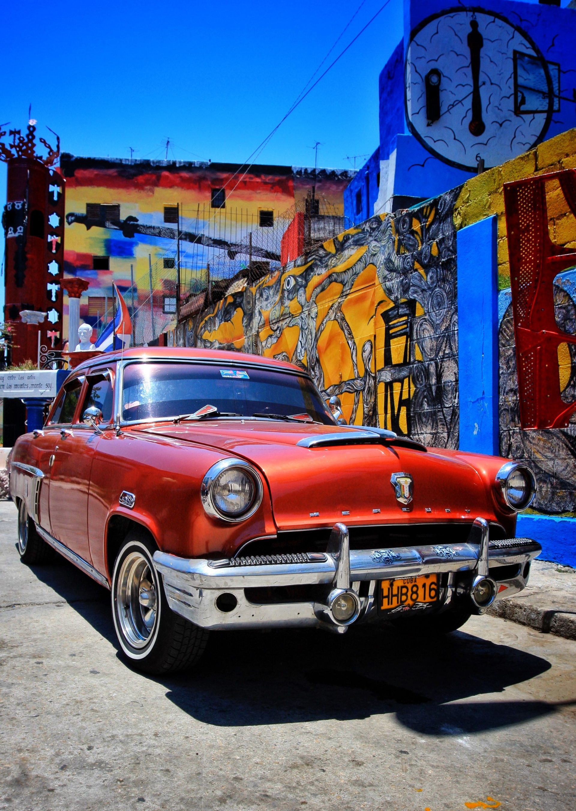 A mural-covered alley in Havana with a vintage red car parked in it
