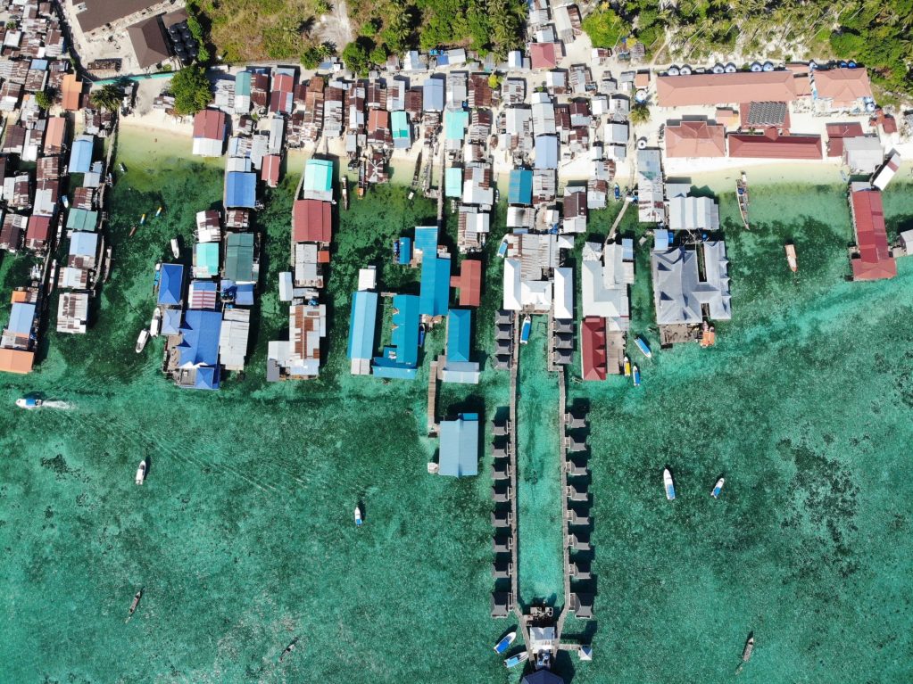 Stunning aerial view of a coastal village in Sabah, Malaysia, with clear turquoise waters and vibrant rooftops.
