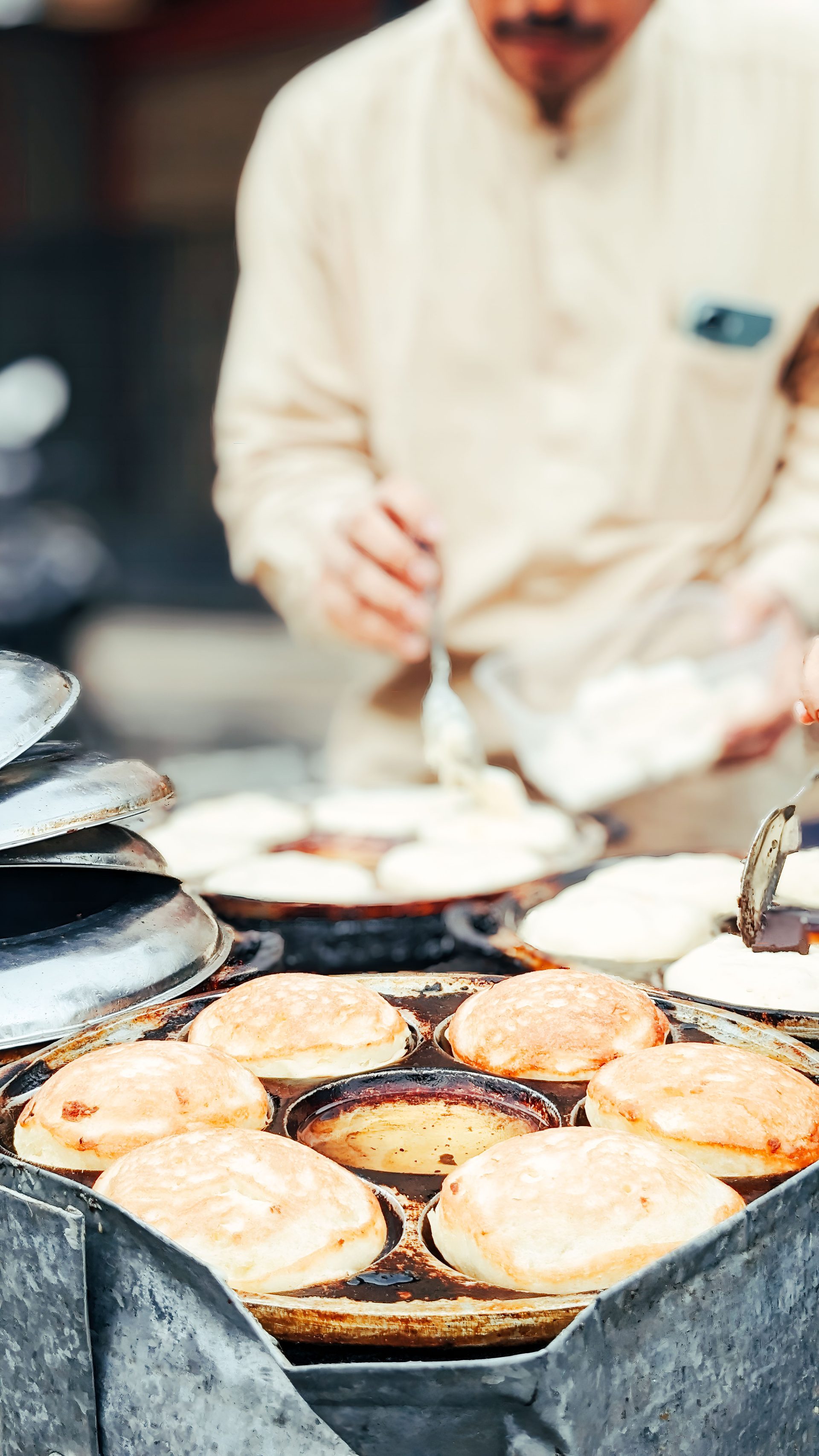 Khanom khrok coconut pancakes cooking in a dimpled iron pan