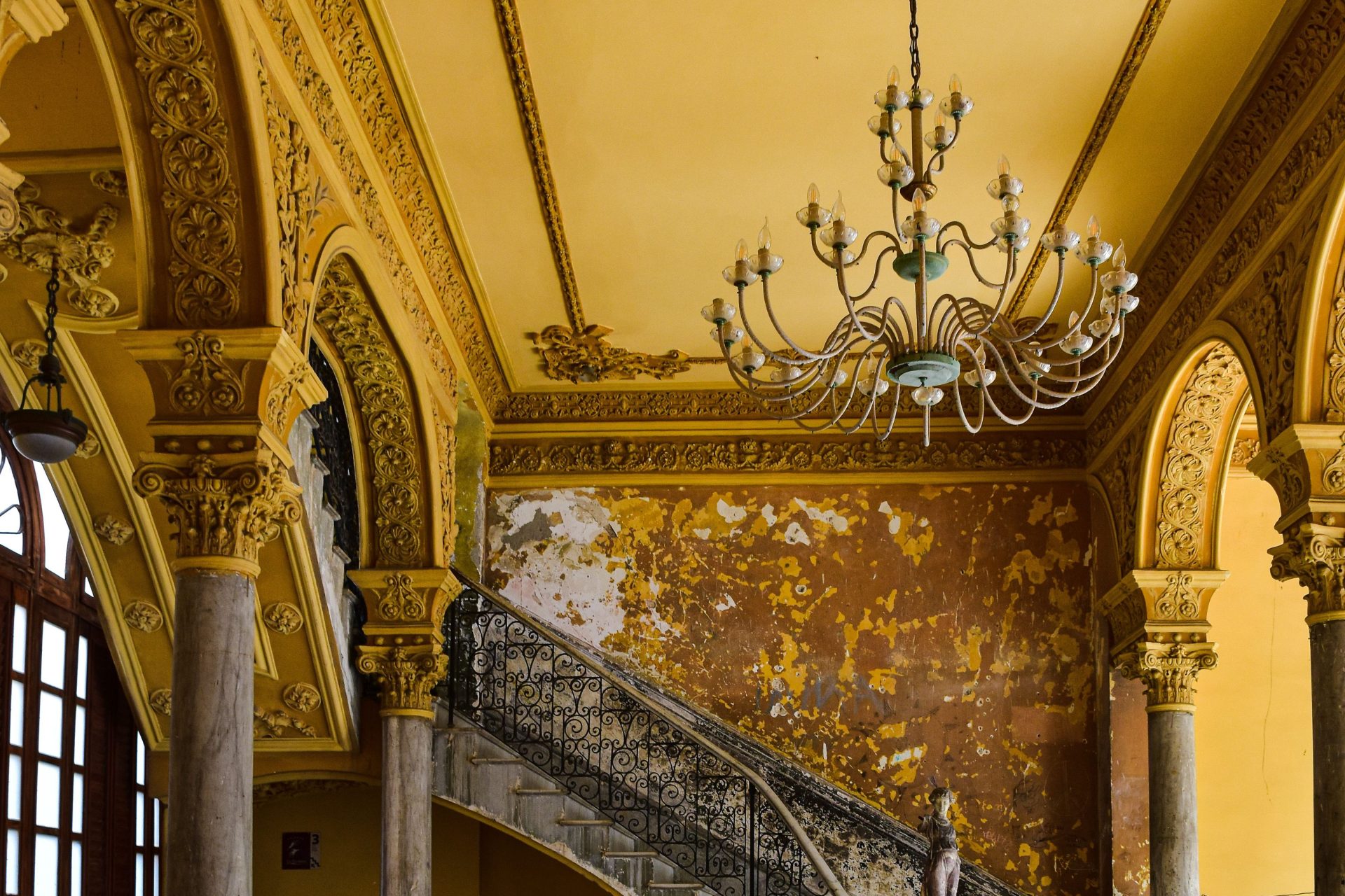 Ornate staircase with chandelier in a historic Cuban mansion, showcasing classic architecture.
