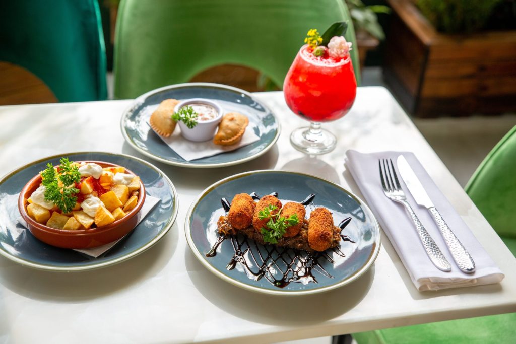 A vibrant spread of cuban  tapas dishes paired with a refreshing cocktail on a sunlit table.