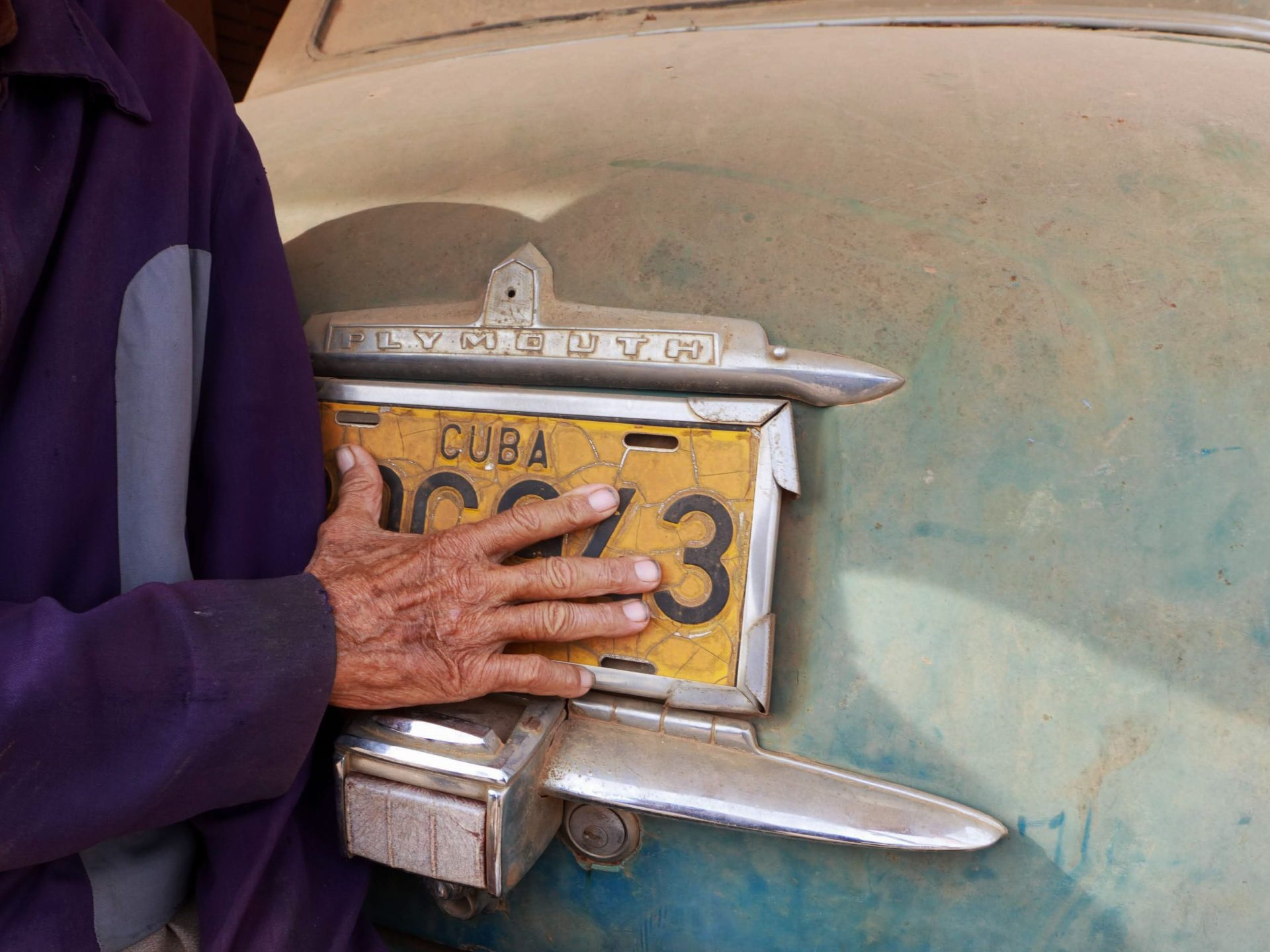 Hands resting on the bonnet of a vintage Cuban car