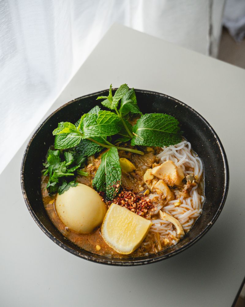 Bowl of mohinga, Myanmar's lemongrass fish noodle soup, with lime and herbs