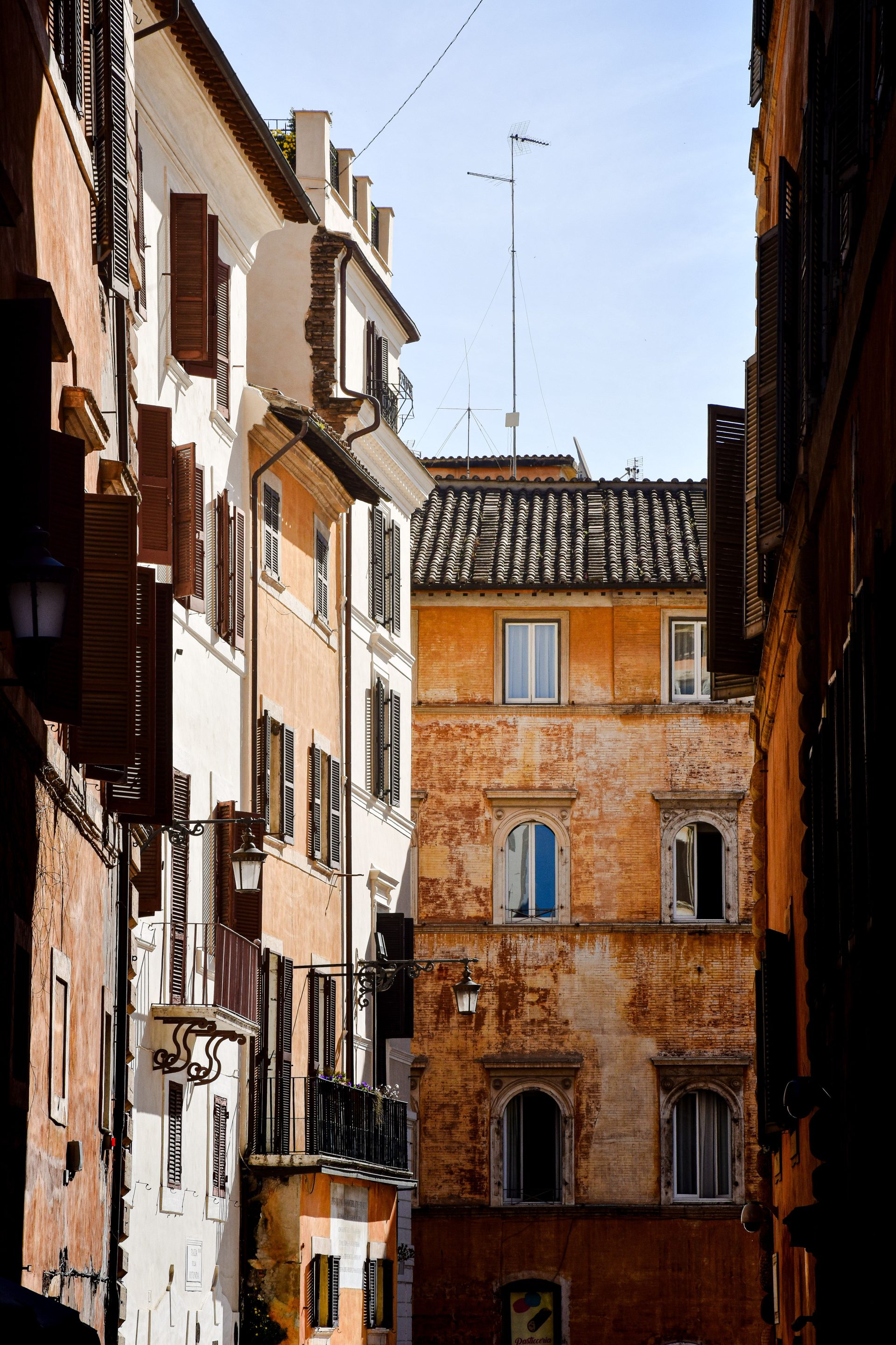 A tall ochre building on a narrow Roman street in warm light