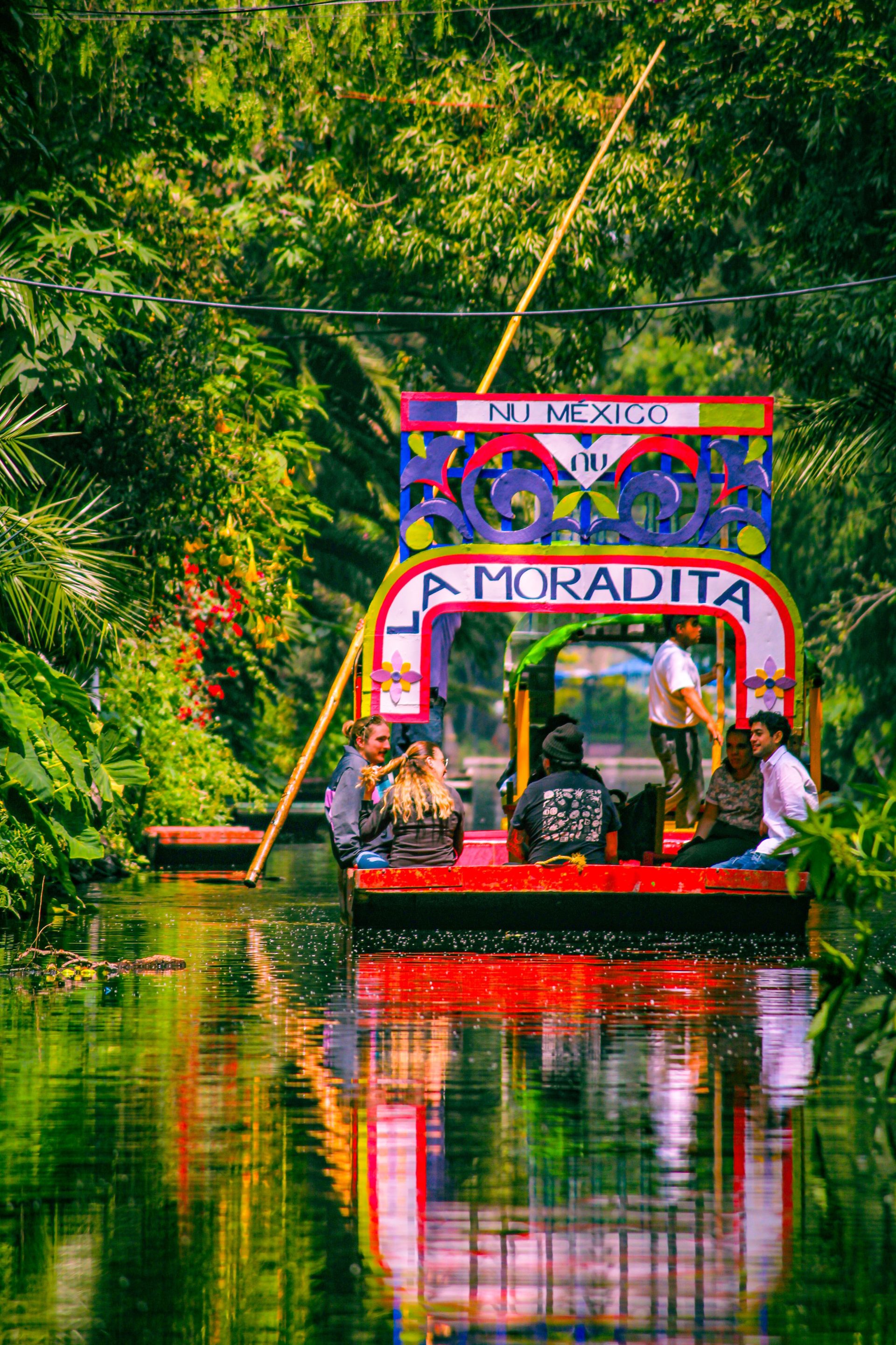 A decorated trajinera boat with a painted arch moving along the Xochimilco canals
