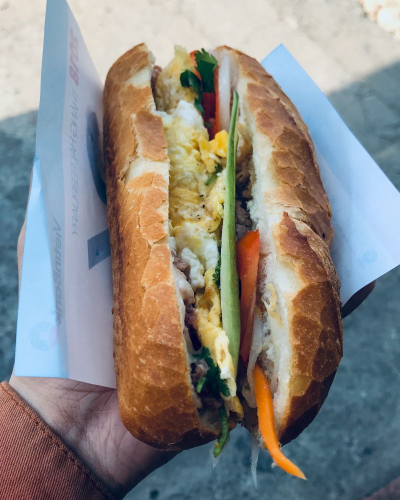 Bánh mì ốp la sandwich with a fried egg, held up close