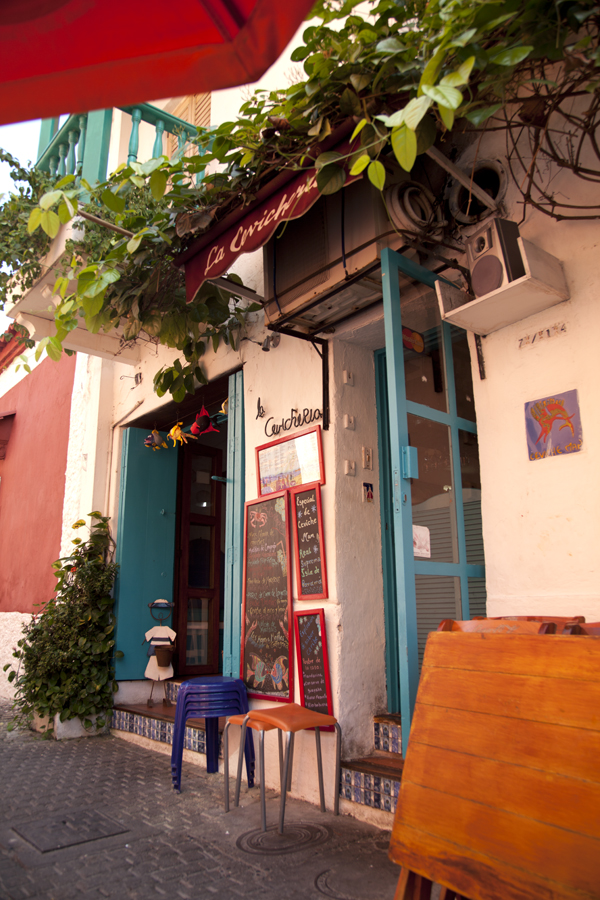 A pink and green painted house front in Getsemani with plants and blue stools outside