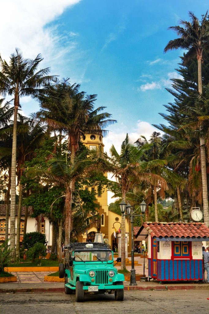 A green Jeep Willys parked on the plaza in Salento beneath tall palms