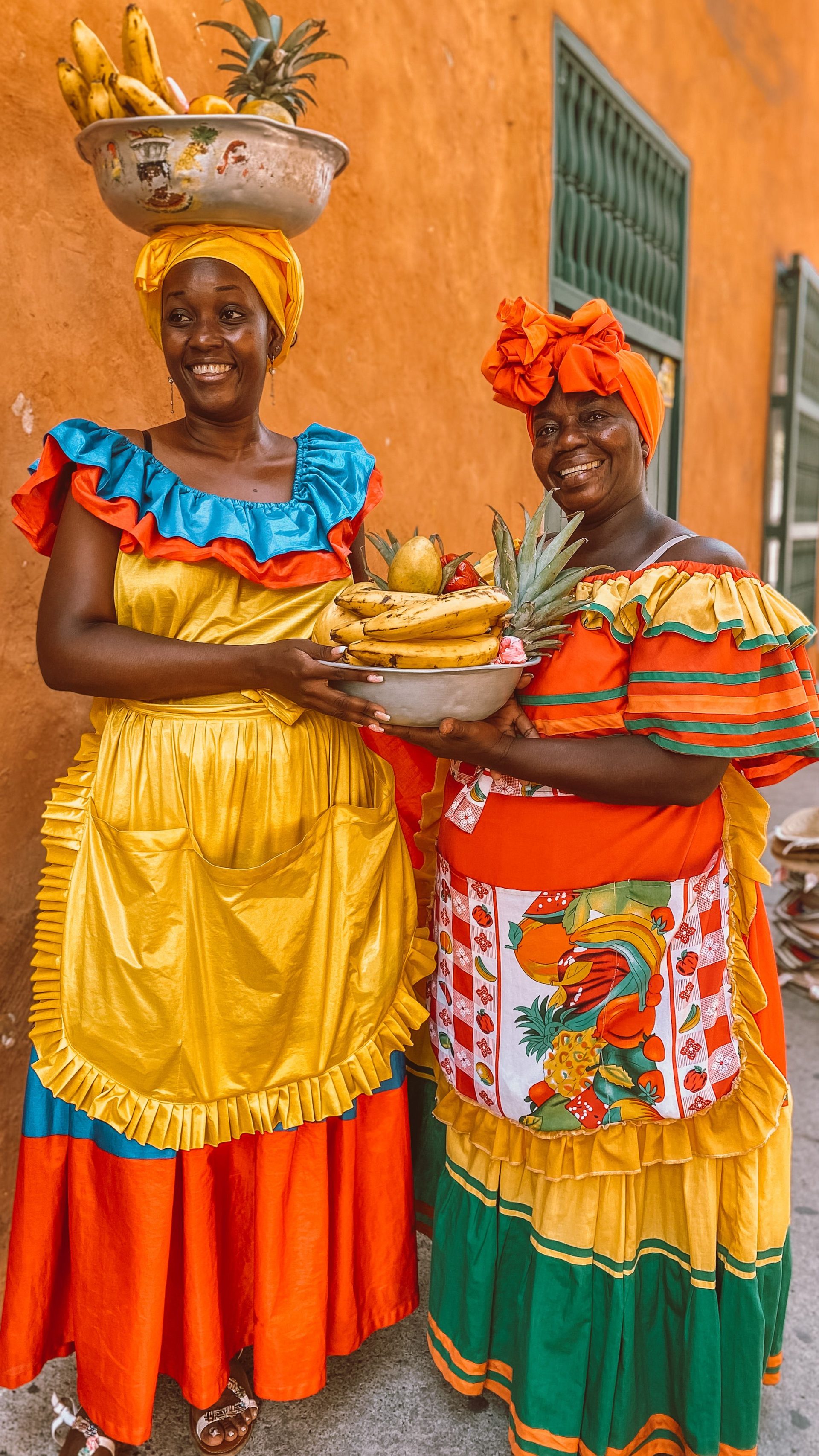 A palenquera in a ruffled dress carrying a bowl of fruit on her head in Cartagena