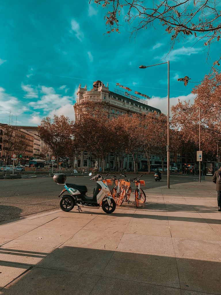 A scooter and a bicycle parked on a wide boulevard in autumn