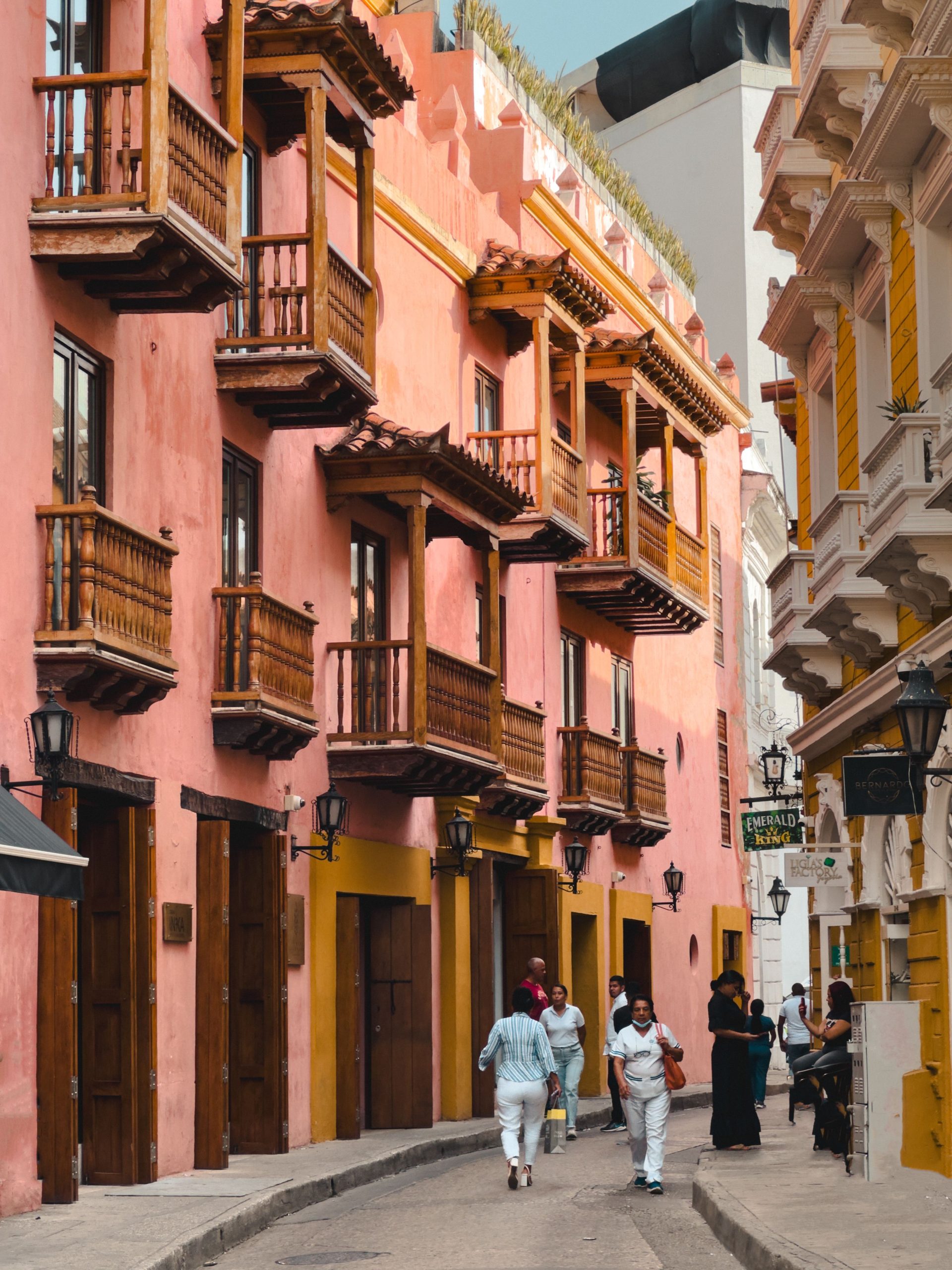 A pink colonial building in Cartagena with carved wooden balconies above a street of shopfronts