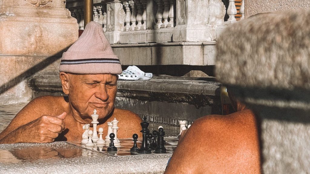 A man playing chess at a steaming outdoor thermal bath