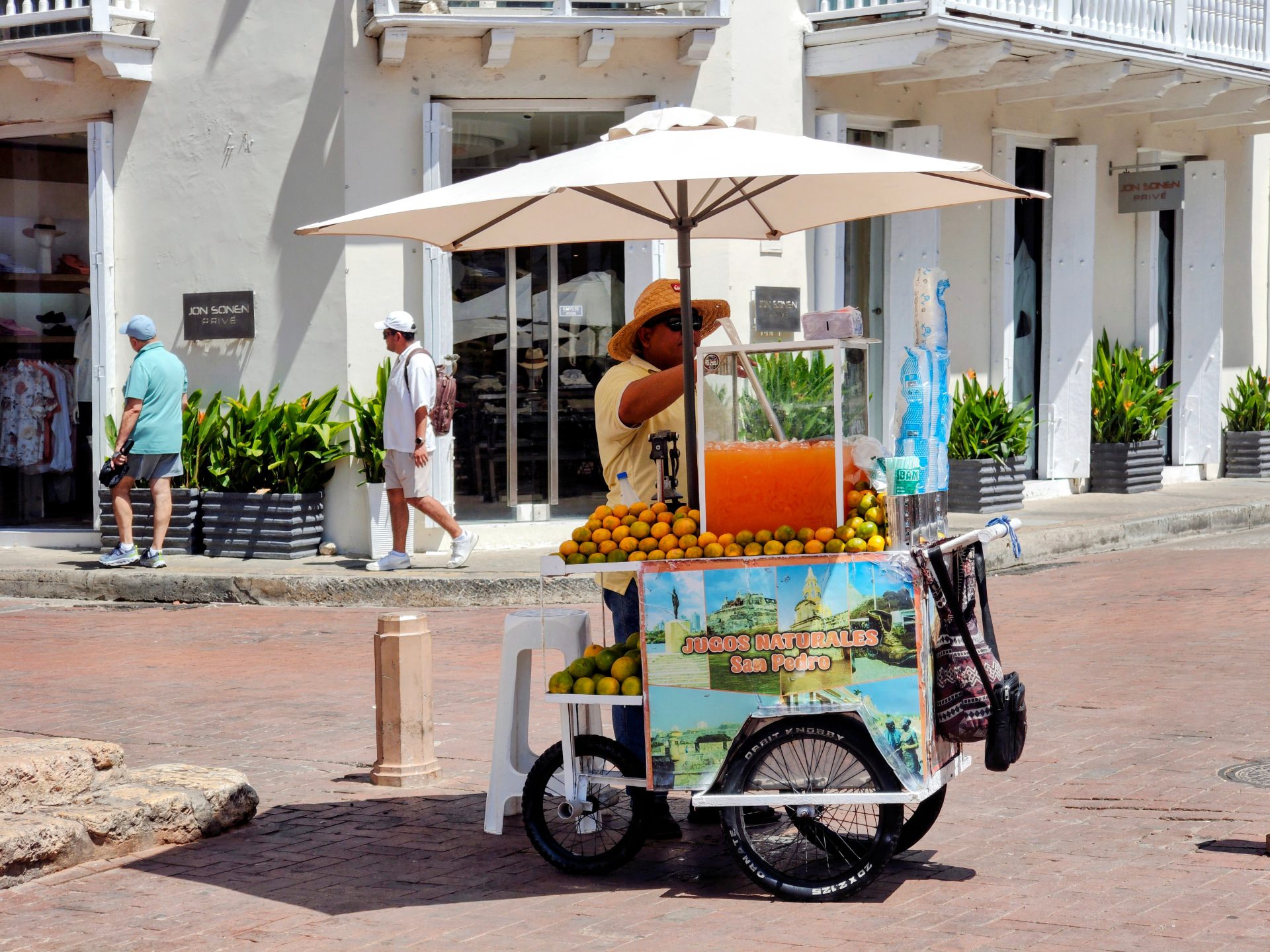 White parasols over tables on a Cartagena street with a tuk-tuk passing