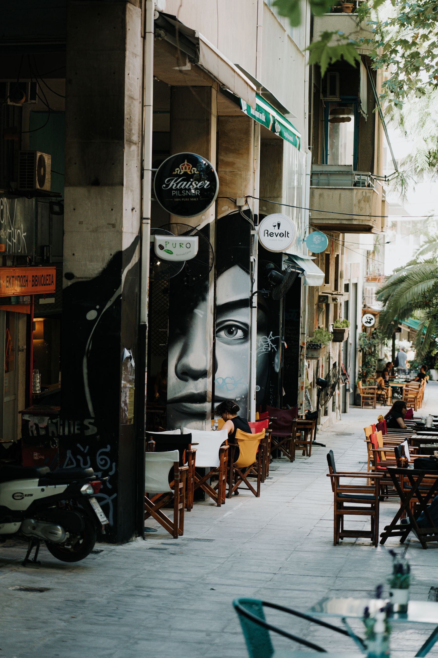 An Athens street with a large mural and parked scooters