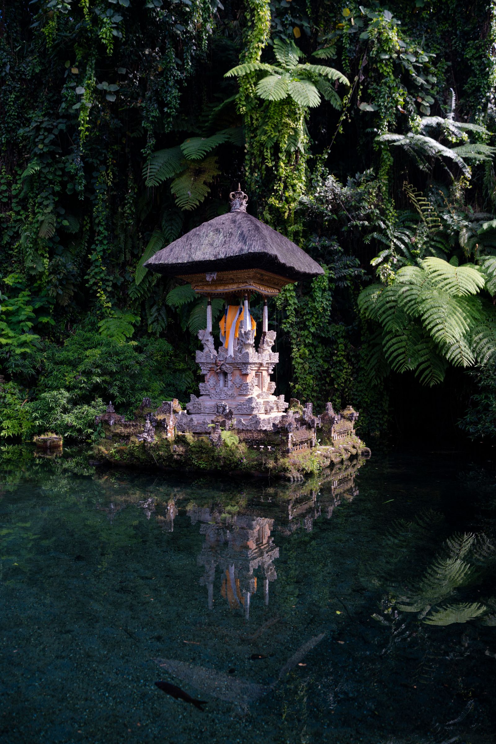 A Balinese water temple surrounded by jungle greenery, reflected in a clear pool