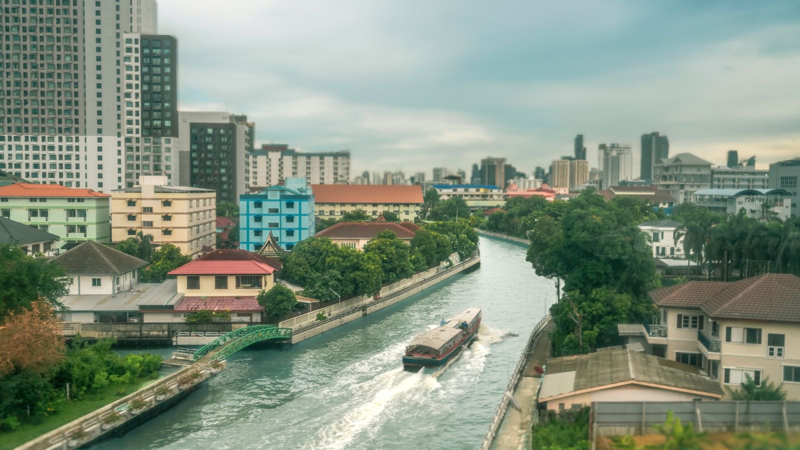 A canal in Bangkok lined with colourful buildings, with a boat passing
