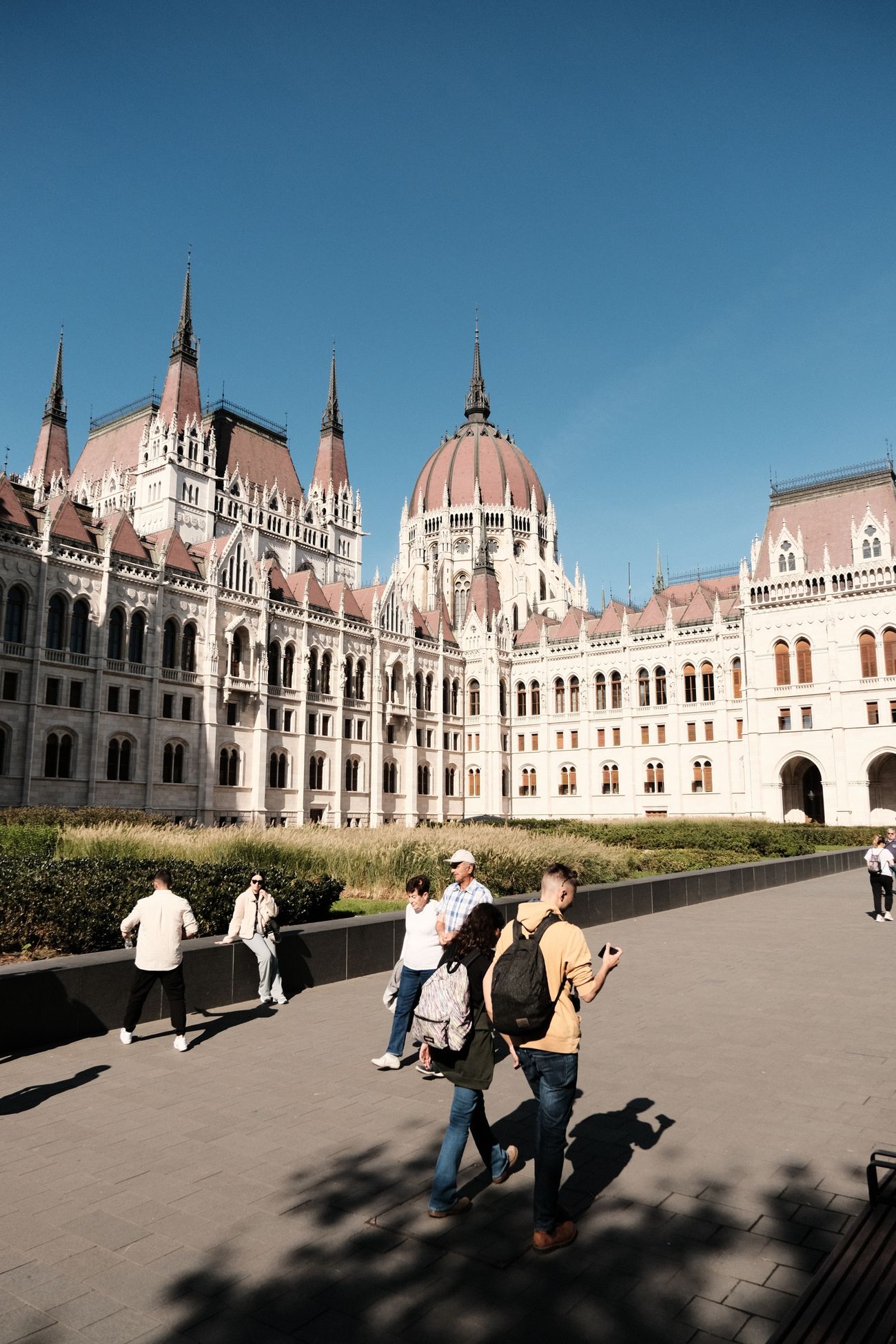 The Hungarian Parliament in daylight with people walking along the promenade