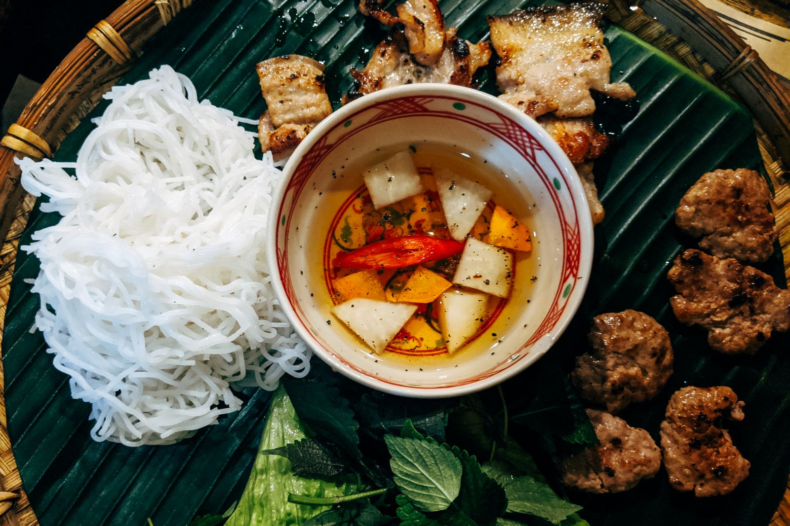 Bun cha with grilled pork, noodles and fresh herbs on a banana leaf