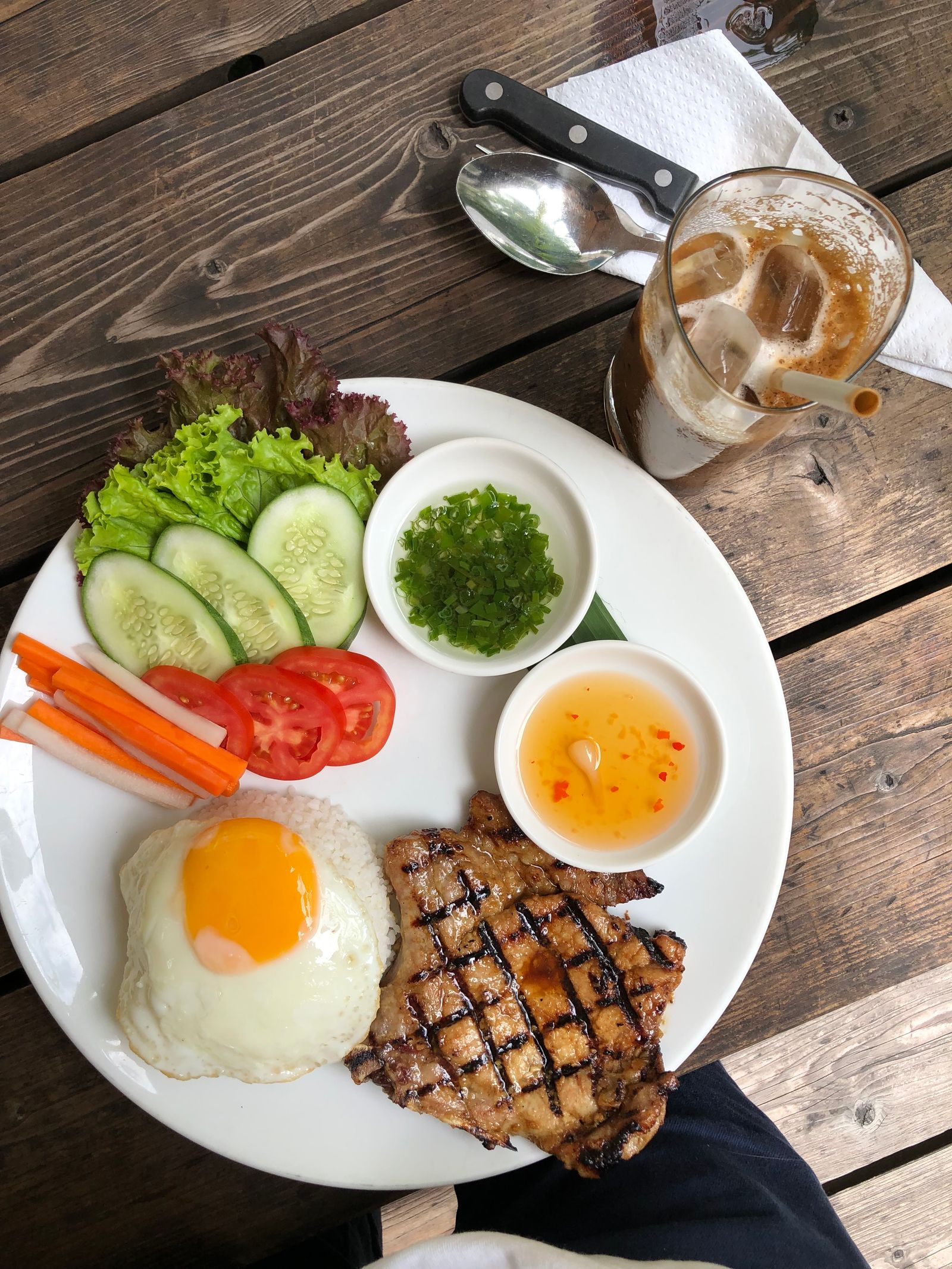 Grilled pork with rice, a fried egg, fresh vegetables and iced coffee