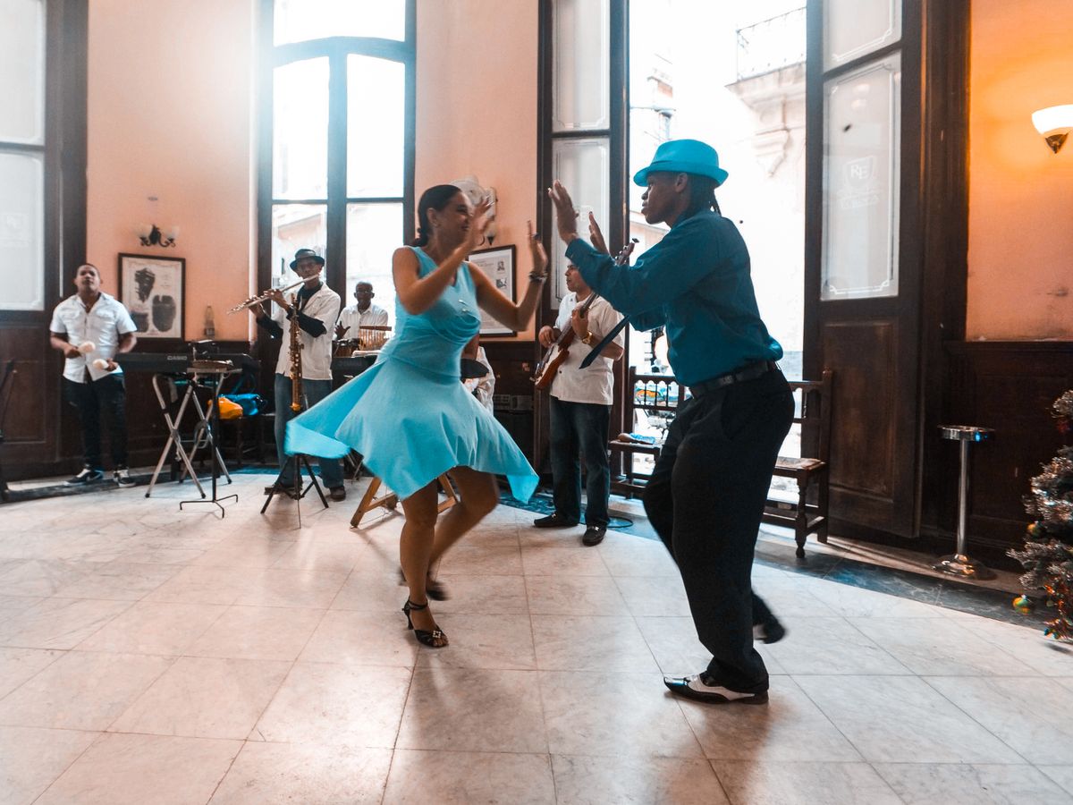 A couple dancing on an open floor in a colonial hall while a live band plays behind them