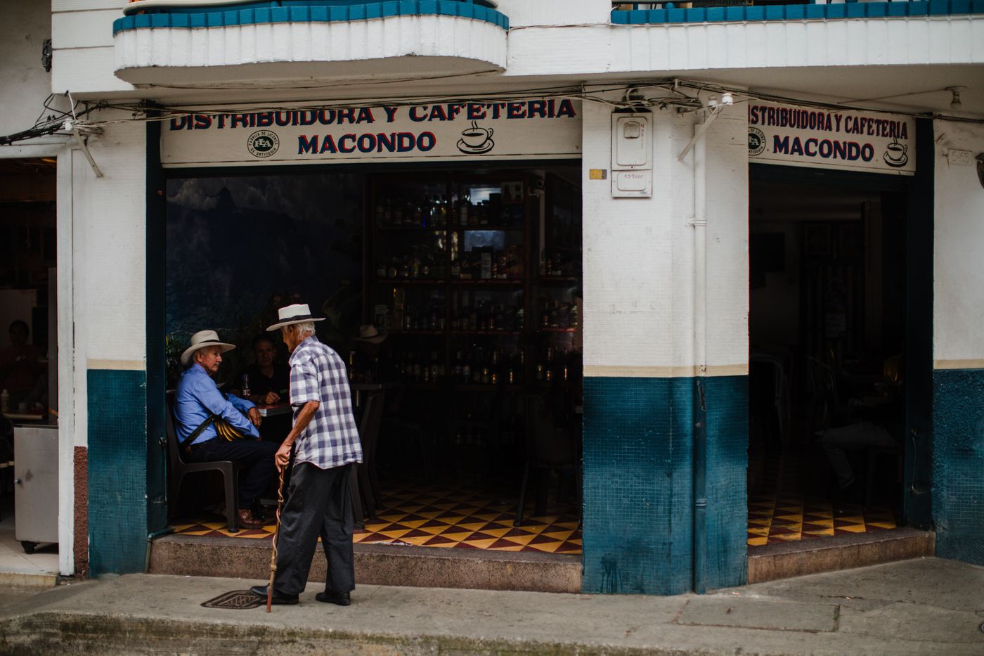 A corner cafeteria in Colombia with men in hats sitting inside and one walking past the tiled facade
