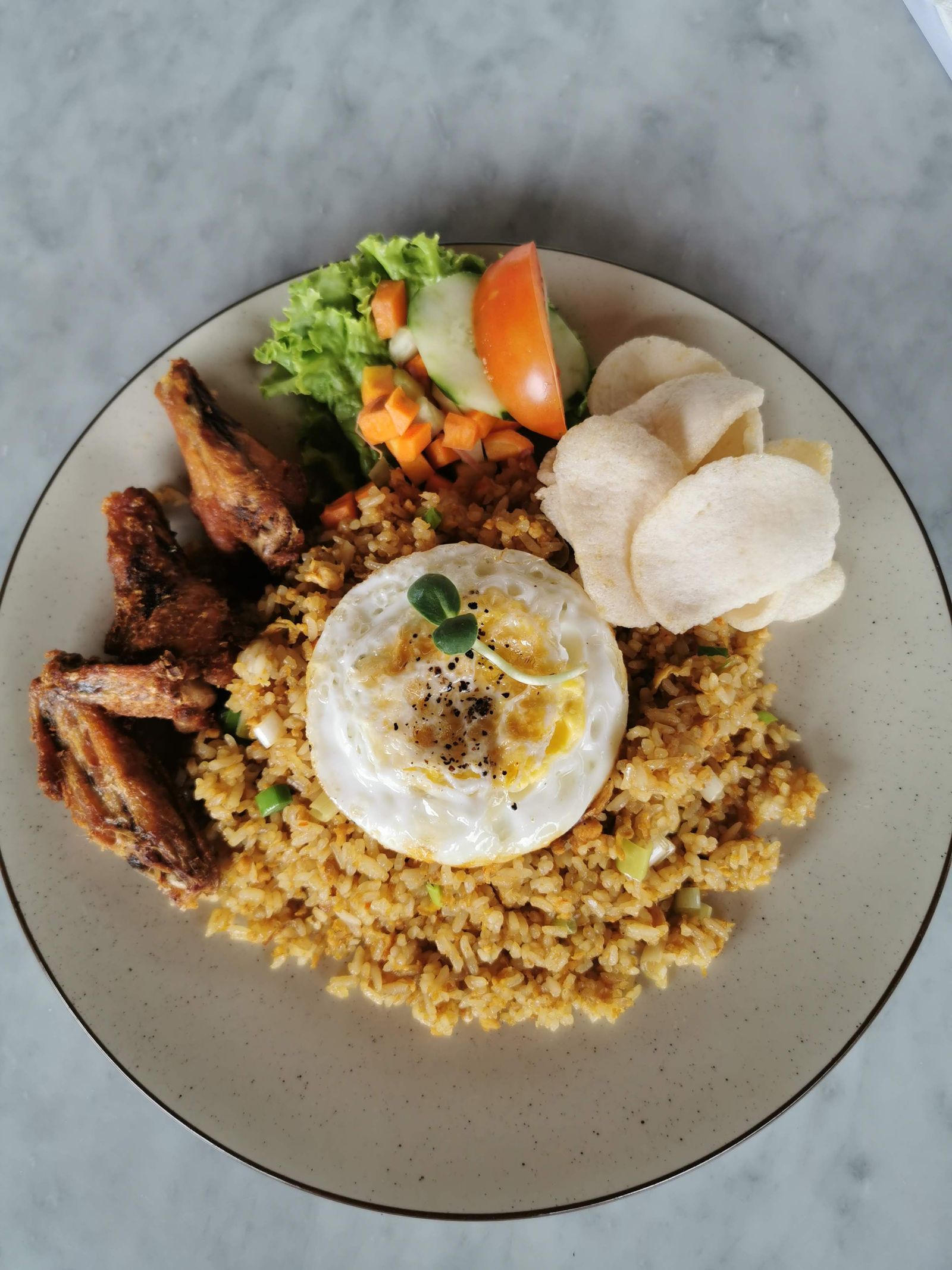 A plate of nasi goreng with fried chicken, egg and vegetables