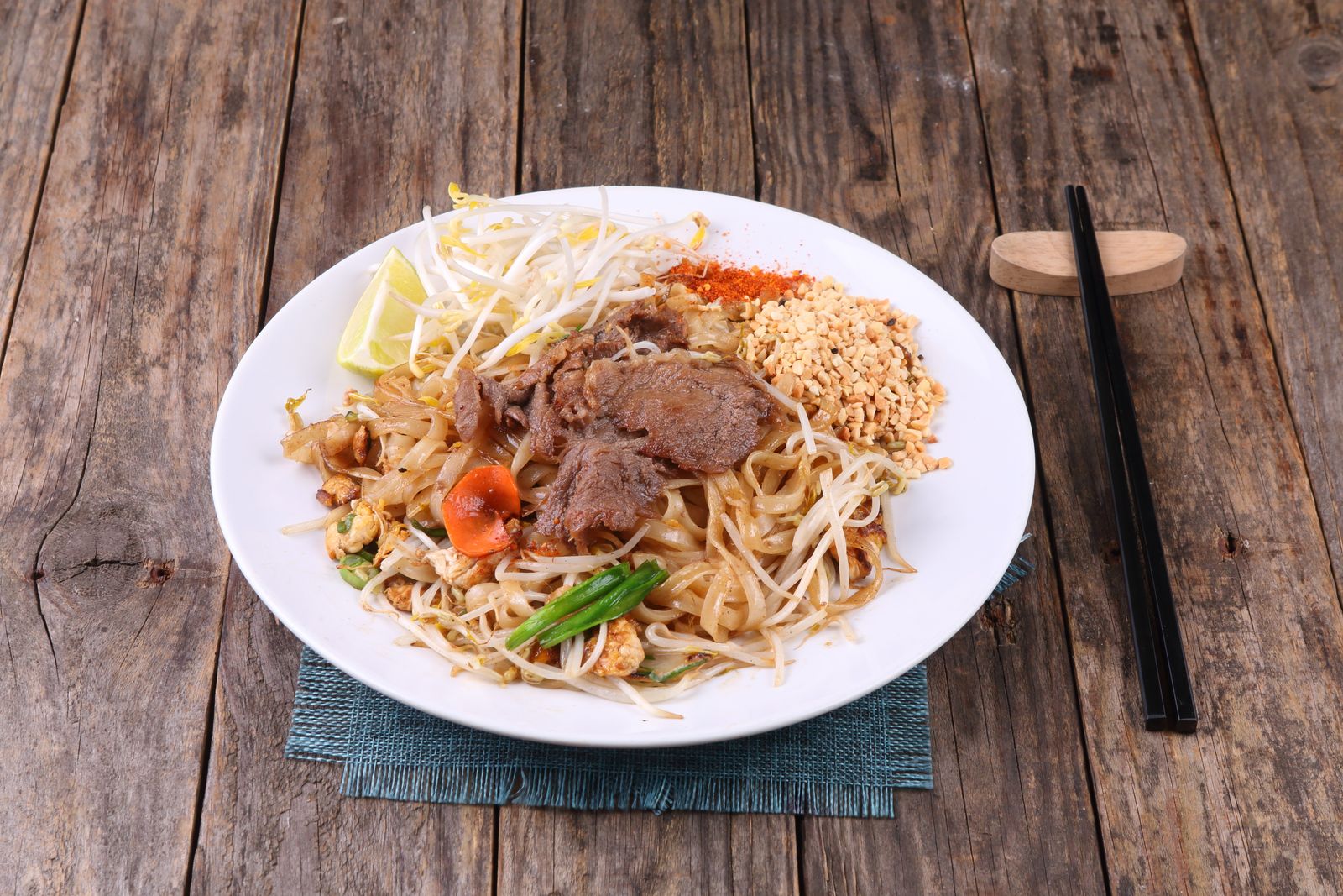Pad thai with beef, peanuts and vegetables on a wooden table
