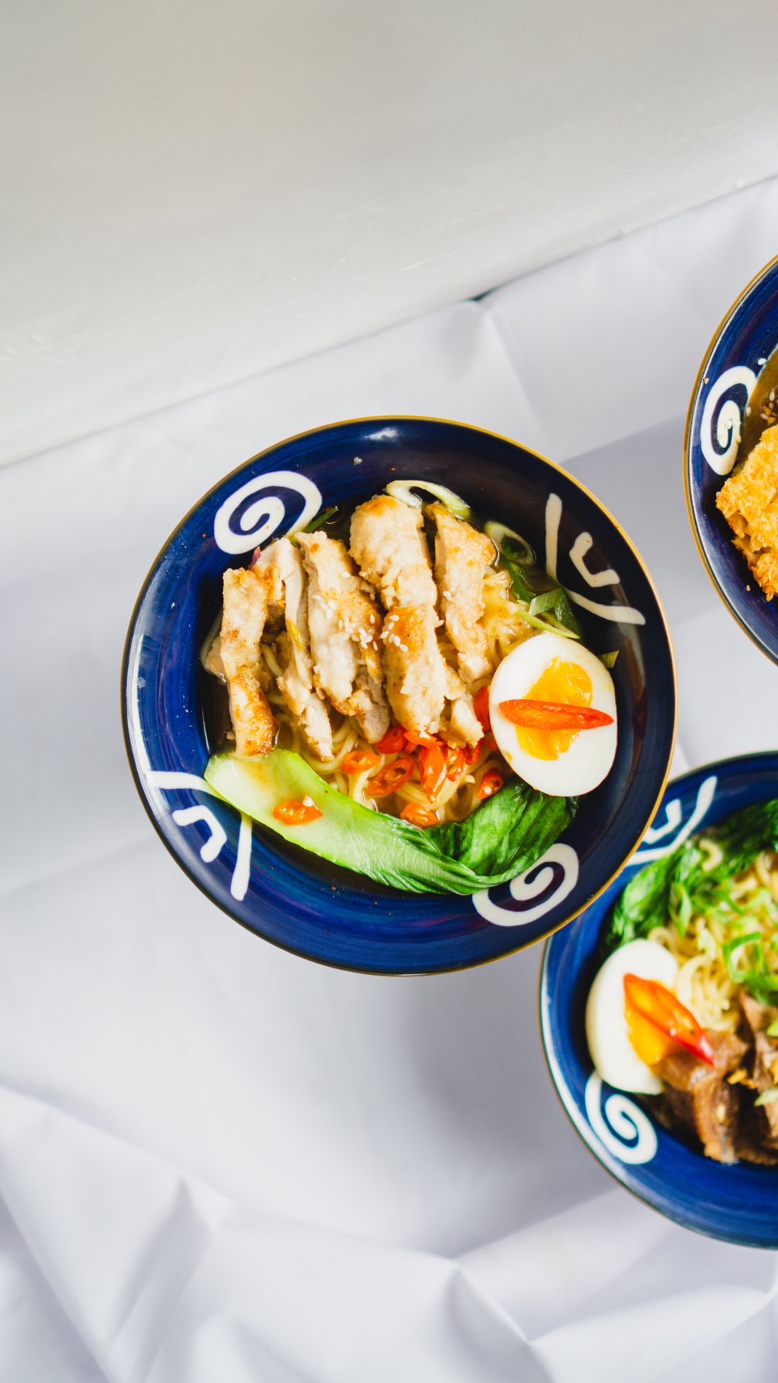 Bowls of ramen with egg and greens photographed from above on a light table