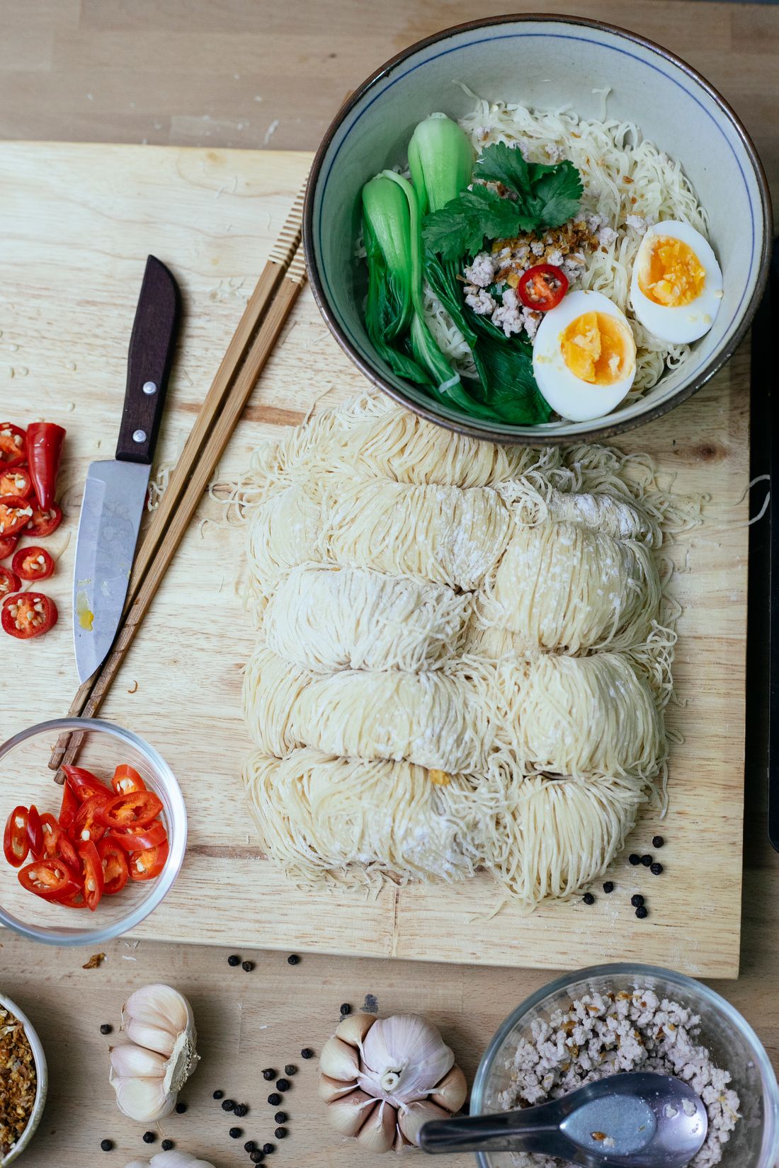 Bundles of fresh ramen noodles laid out beside egg and chilli