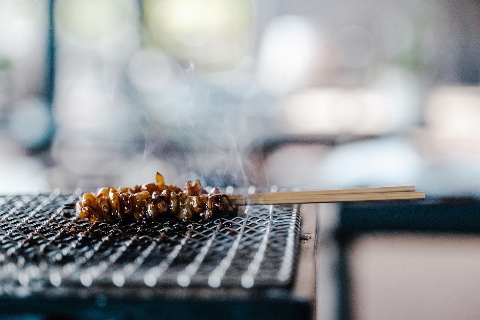Skewered meat sizzling on a grill with smoke rising