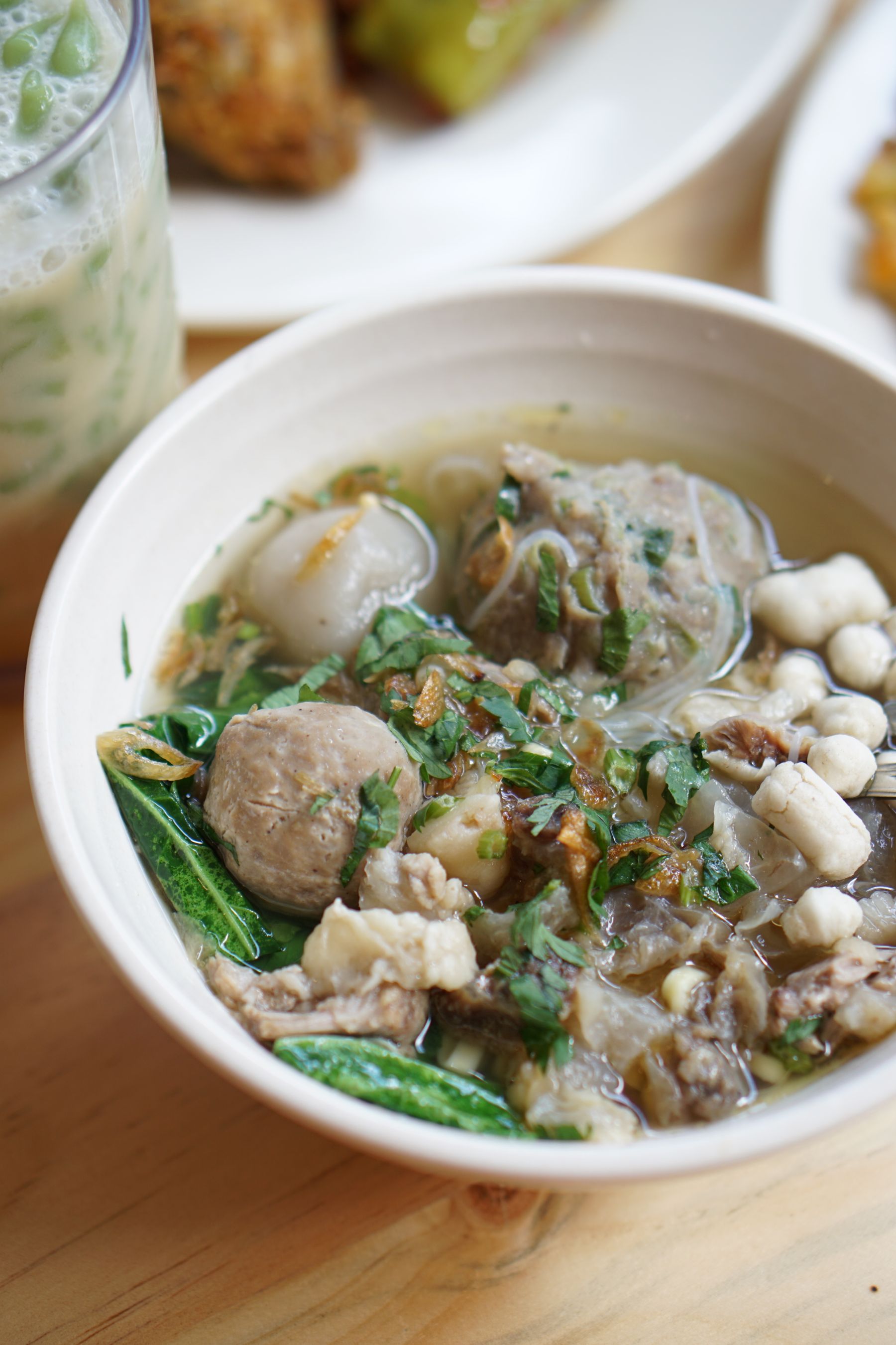 Meatballs in clear broth with greens and noodles in a white bowl