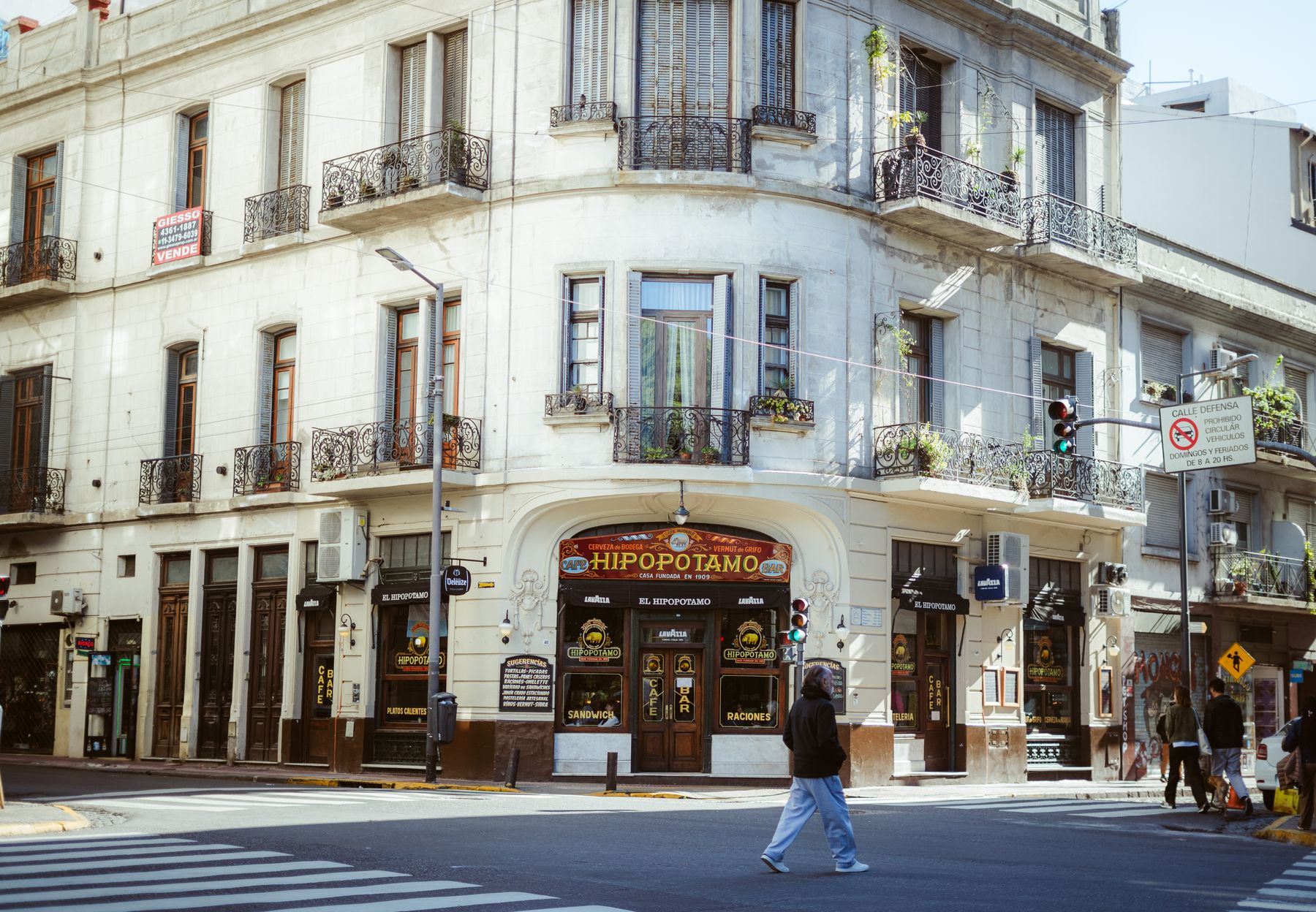 A busy street corner in Buenos Aires with a classic corner cafe and pedestrians