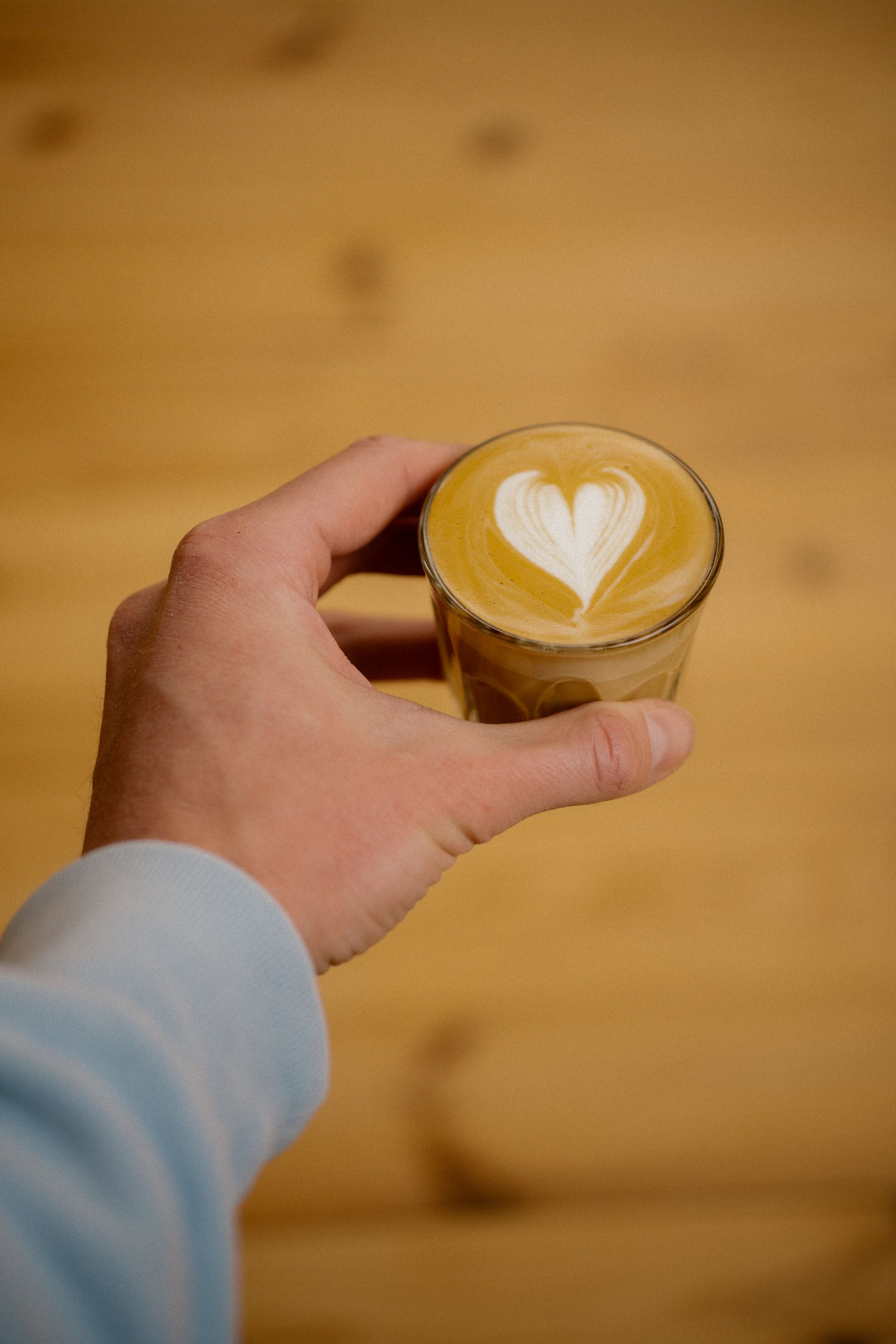 A hand holding a cortado coffee with latte art on a wooden table