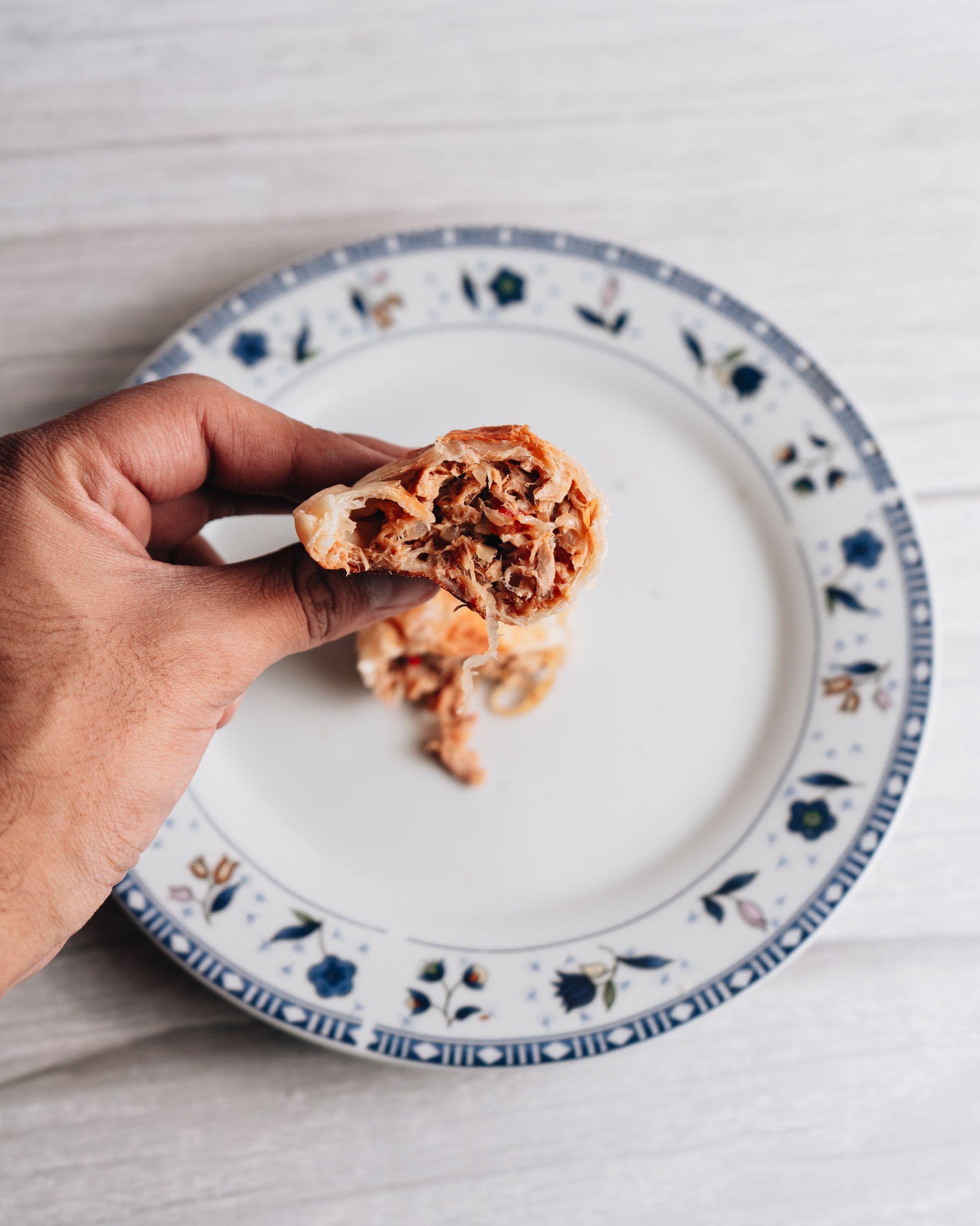 A hand holding a beef empanada on a decorative plate