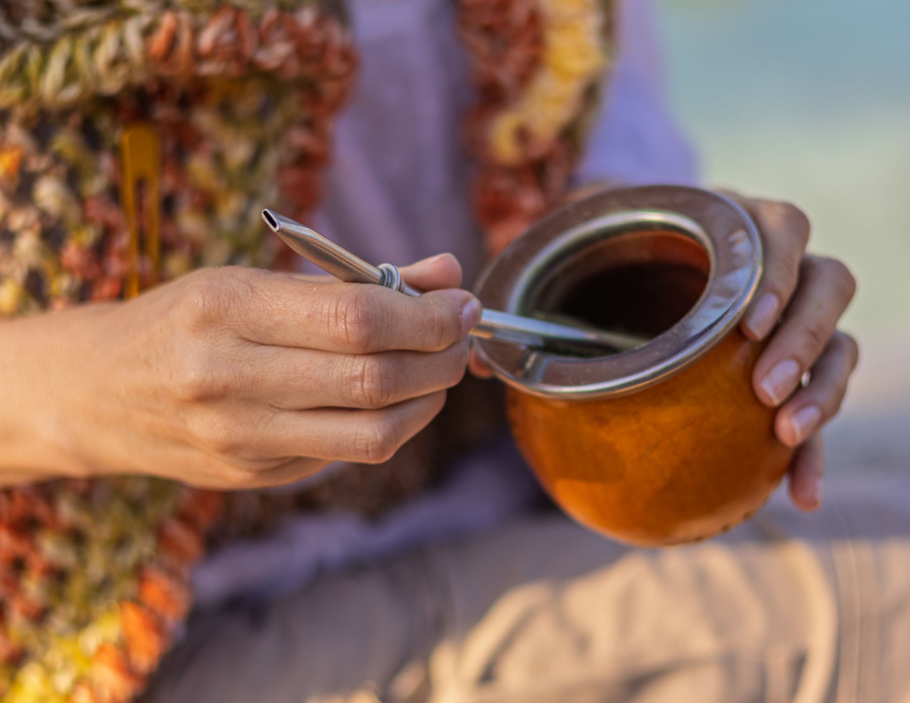 A person holding a traditional mate gourd with a metal bombilla straw
