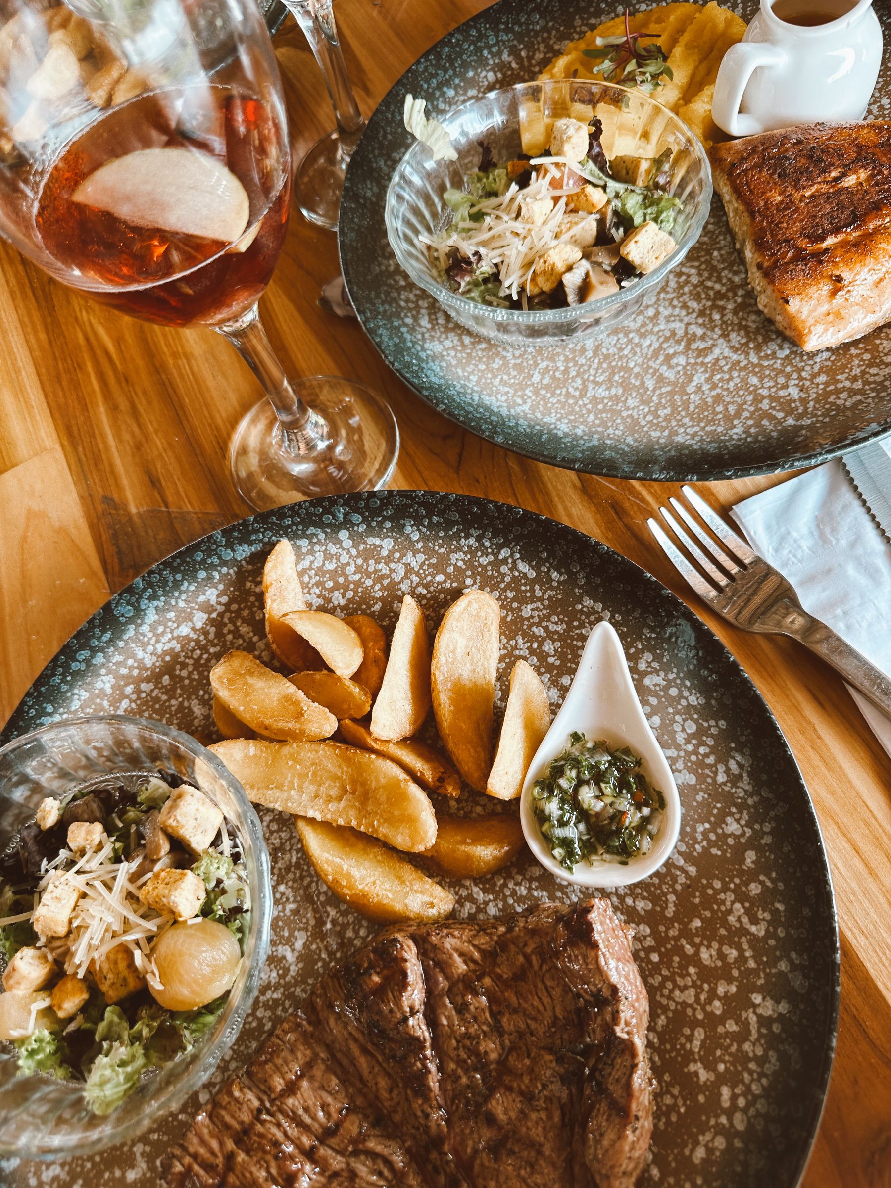 A plate of steak, chips and salad with a glass of red wine on a rustic table