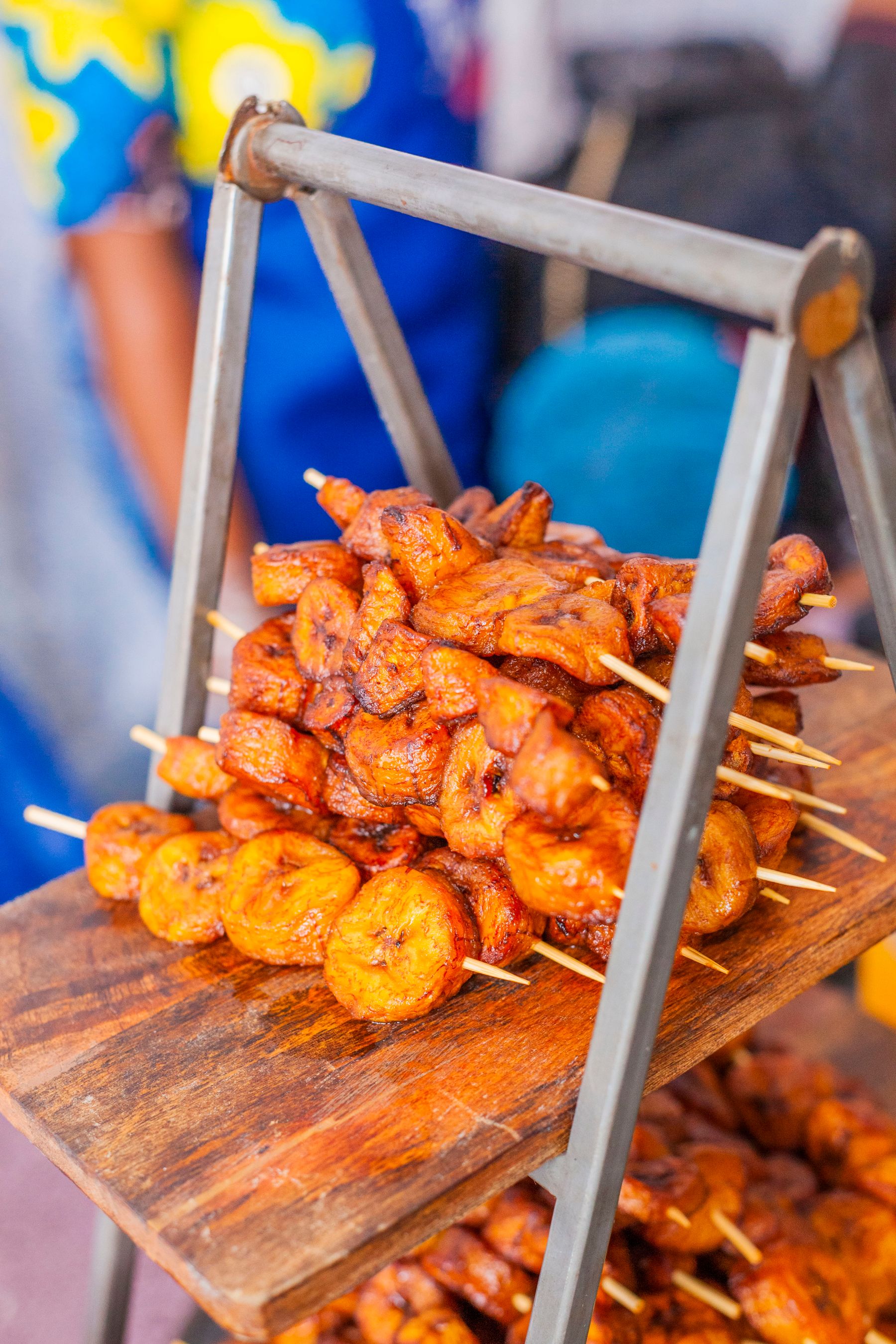 Grilled plantain skewers stacked on a wooden stand at a food stall