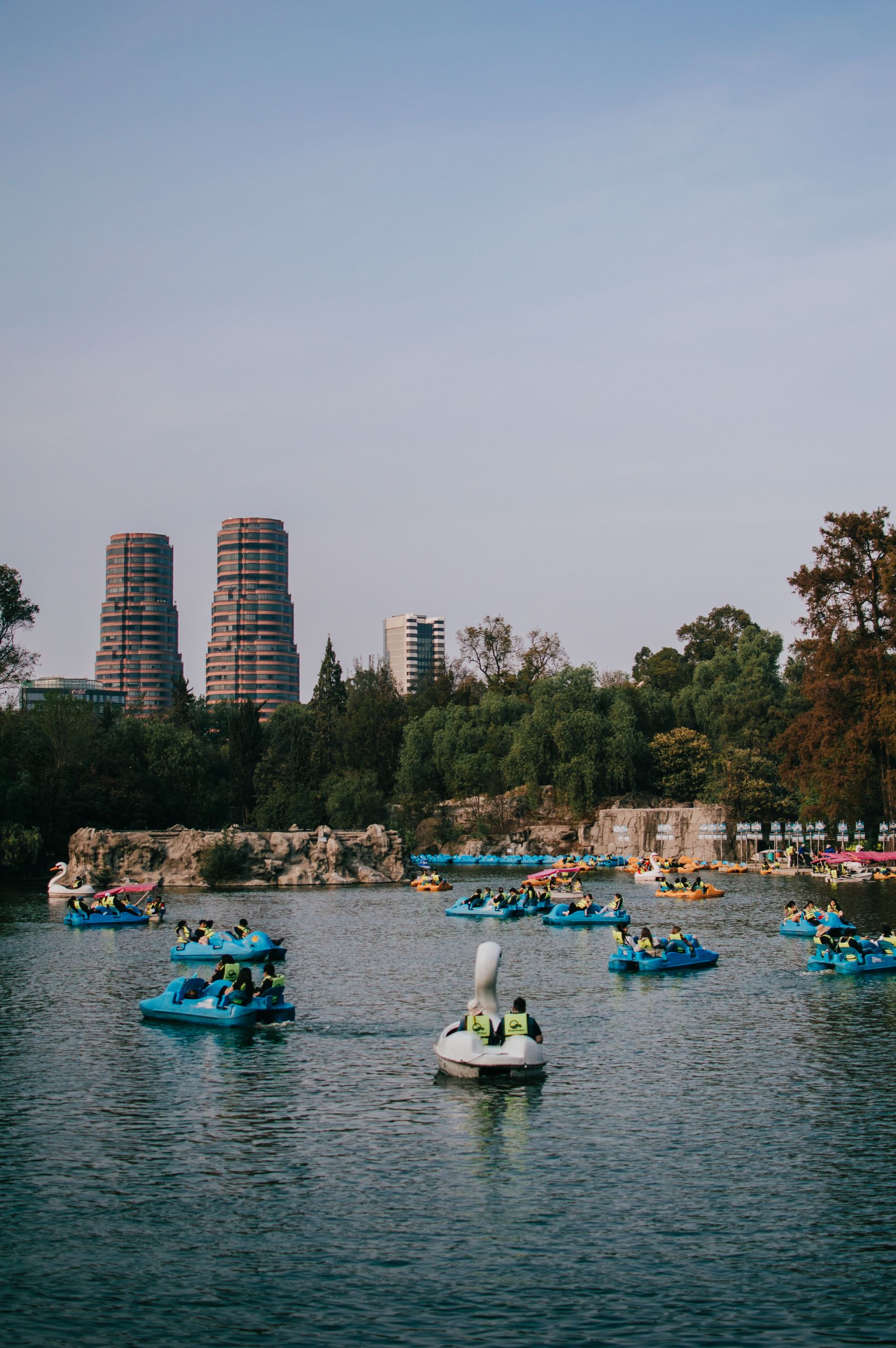 People with paddle boats on the lake in Chapultepec Park with the Mexico City skyline behind