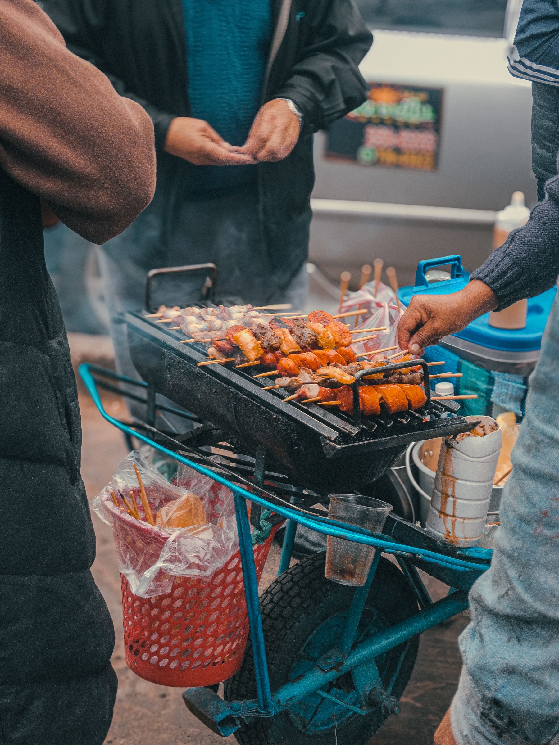 A street vendor grilling meat skewers over a portable charcoal barbecue