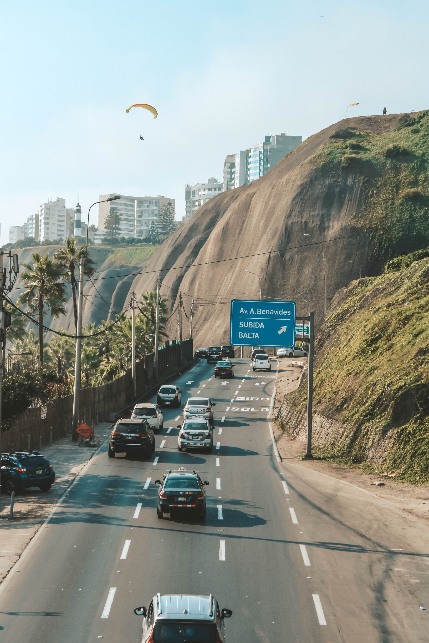 Traffic on a coastal avenue in Lima with cliffs and paragliders behind