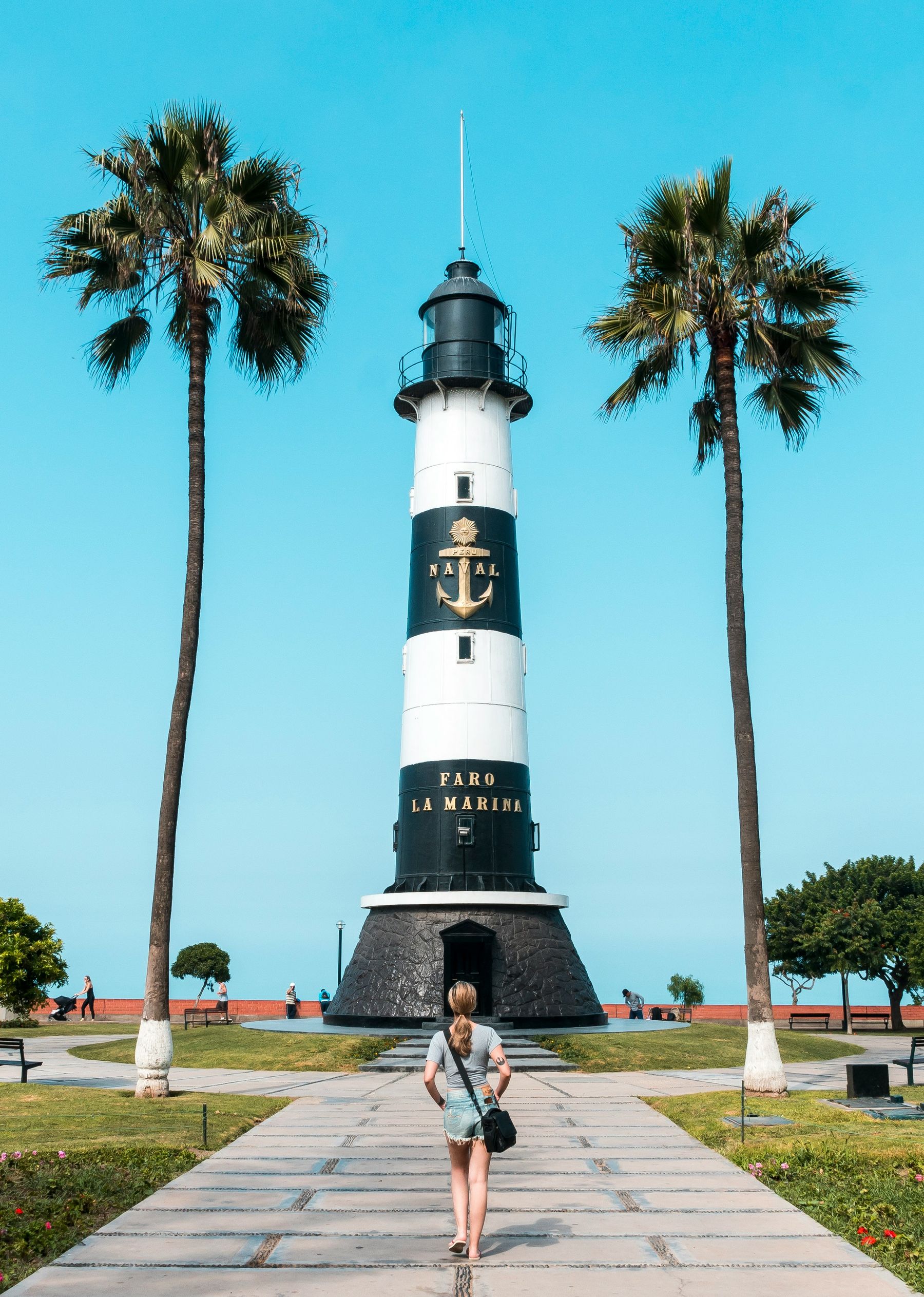 A woman walking towards the Faro la Marina lighthouse framed by palm trees in Miraflores