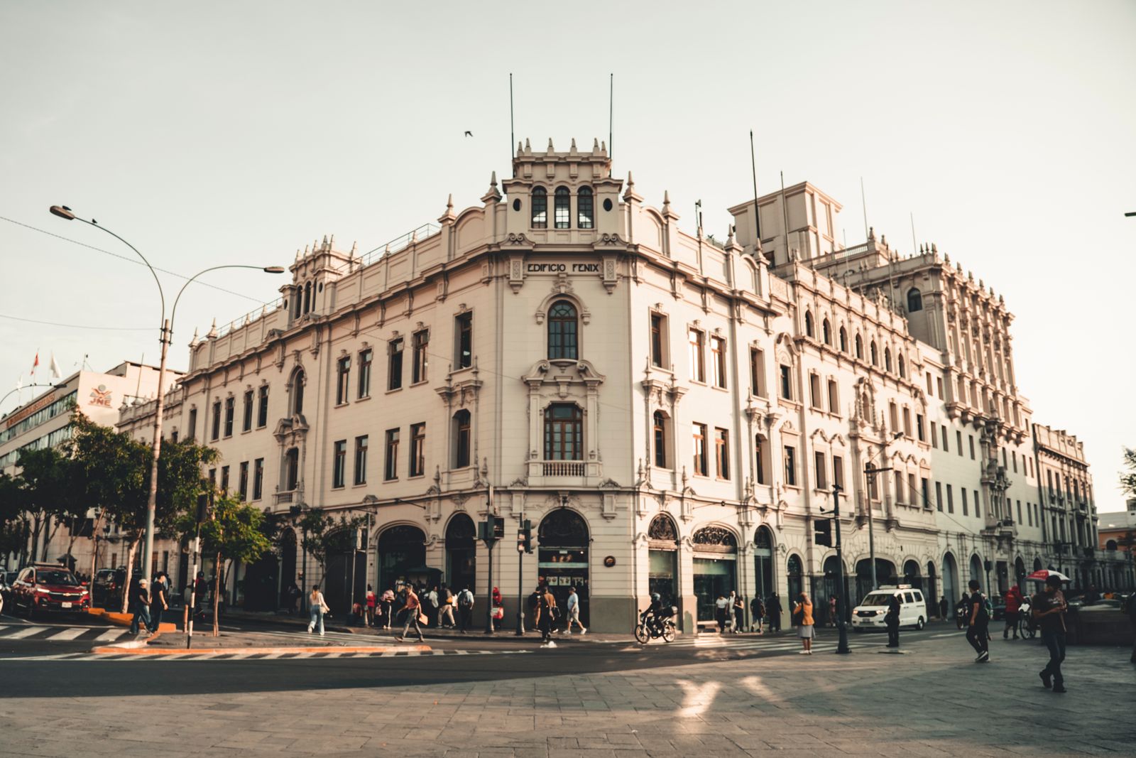 Pedestrians on a bustling Lima street at sunset beside the historic Edificio Fenix