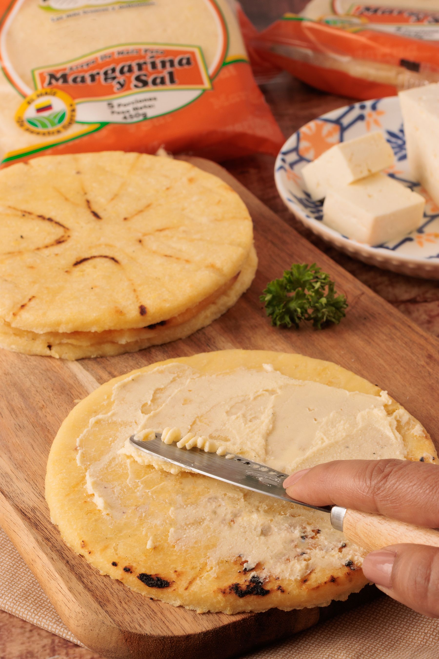A Colombian arepa being prepared with butter and fresh cheese on a griddle