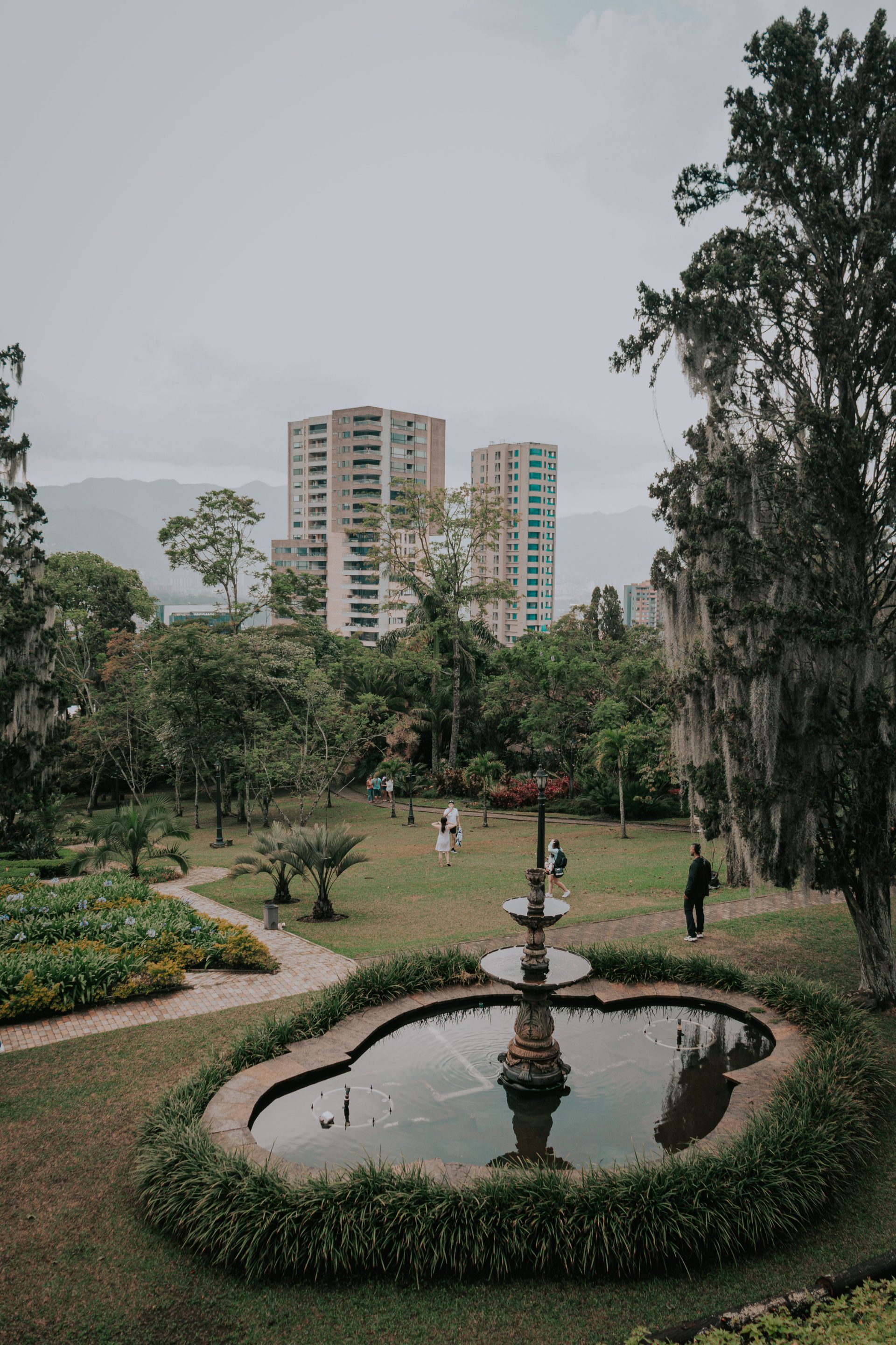 A green park with a fountain and an apartment tower behind it in Medellín