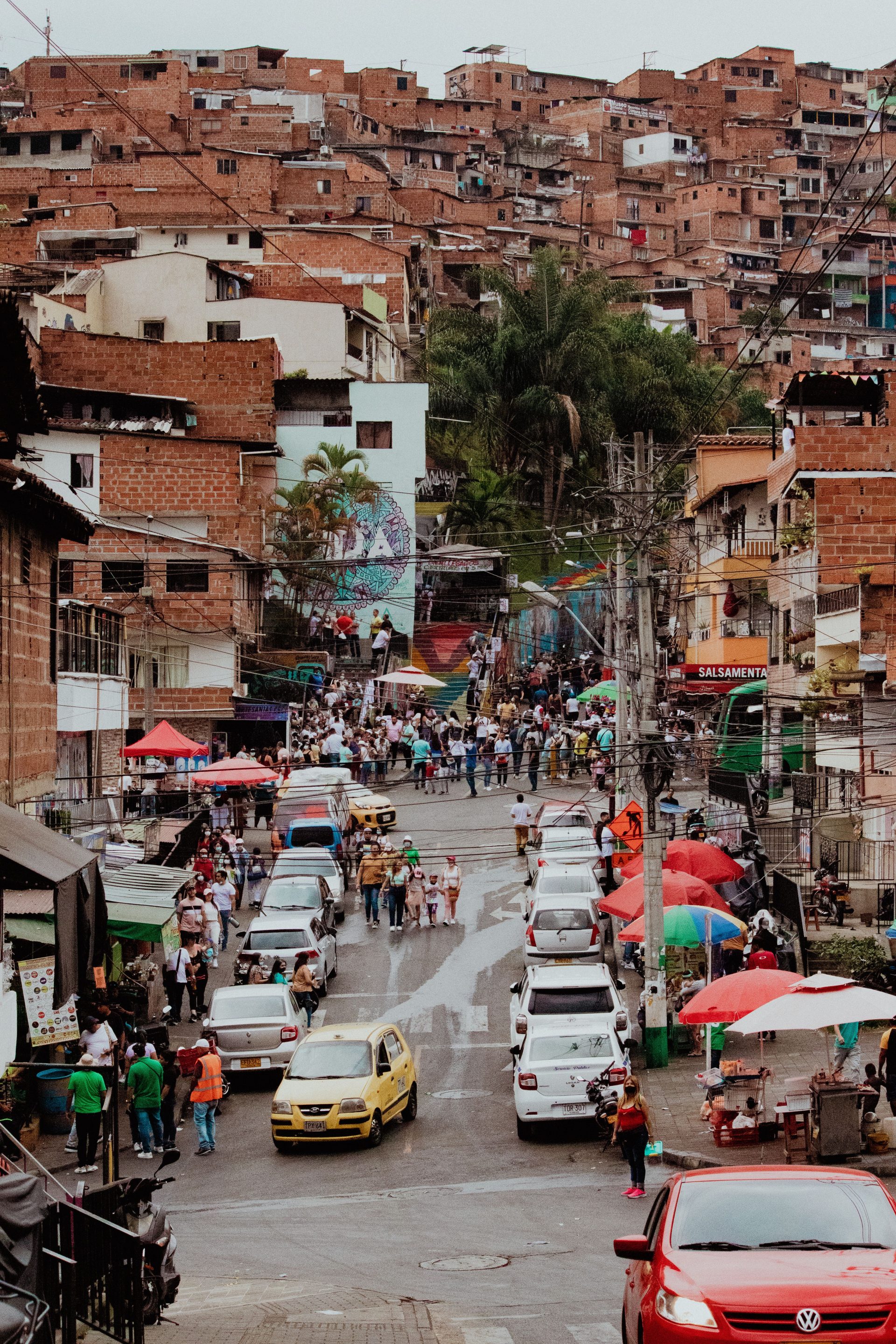 A crowded neighborhood street in Medellín lined with shops and cars