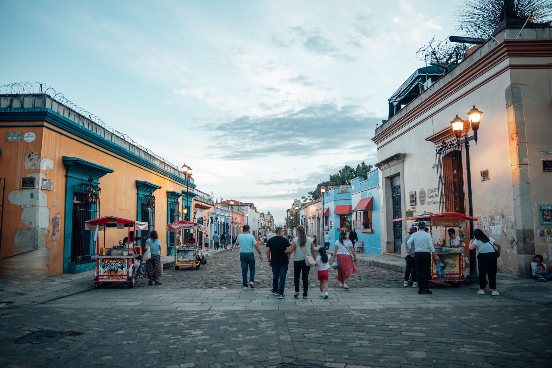 An evening street scene in Oaxaca City with people strolling past colourful architecture